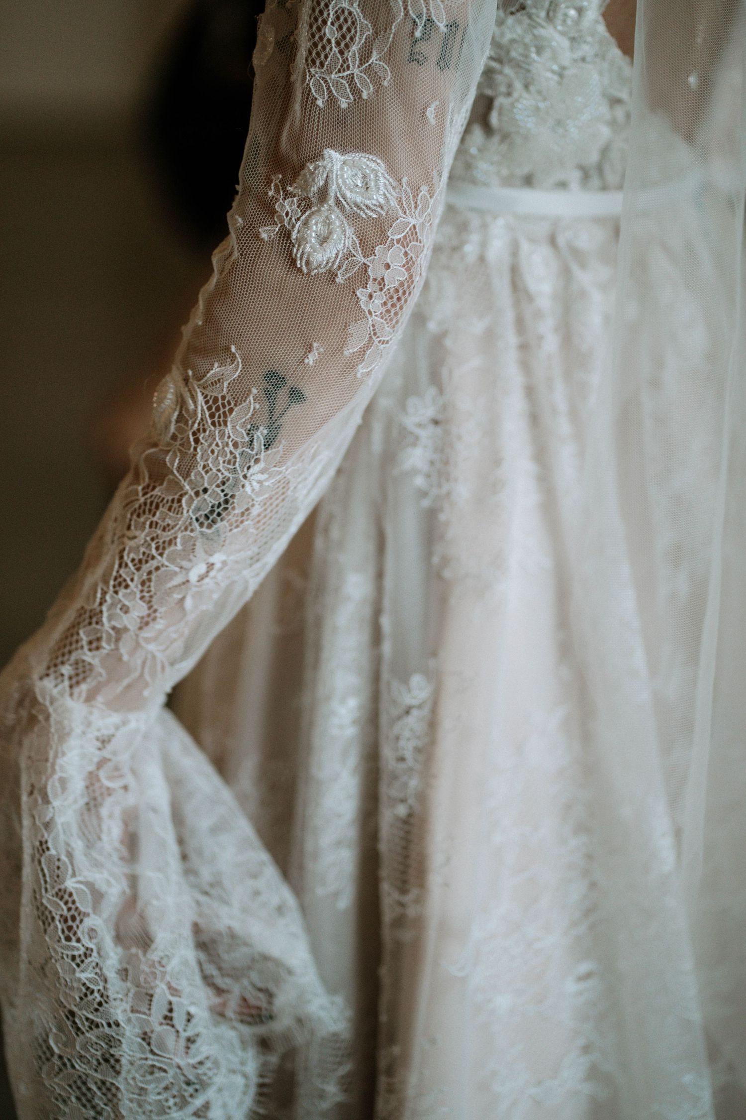 Close-up of an elegant lace wedding dress with long sheer sleeves featuring intricate floral embroidery.