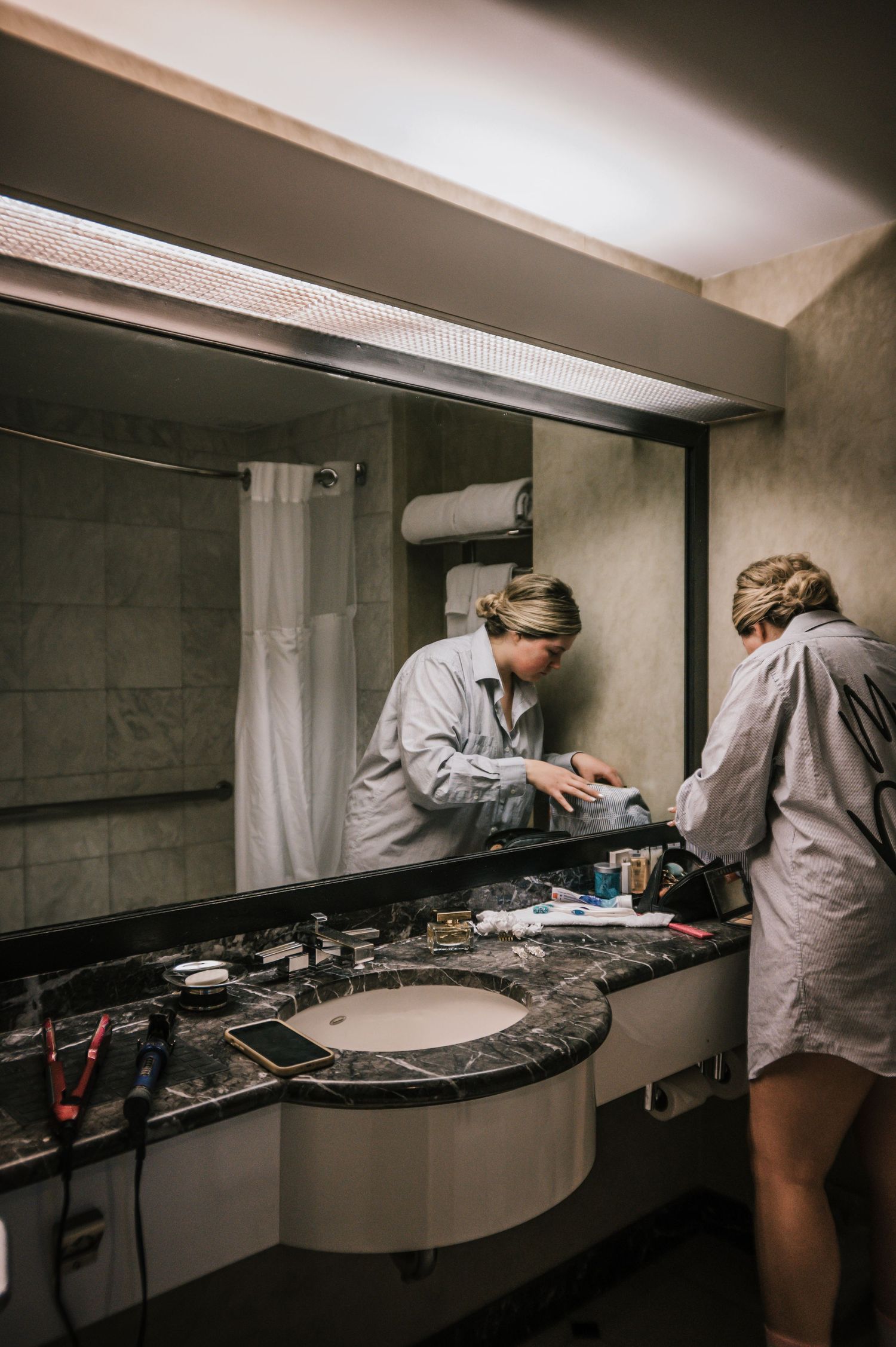 Bride getting ready at hotel bathroom vanity mirror before wedding ceremony.