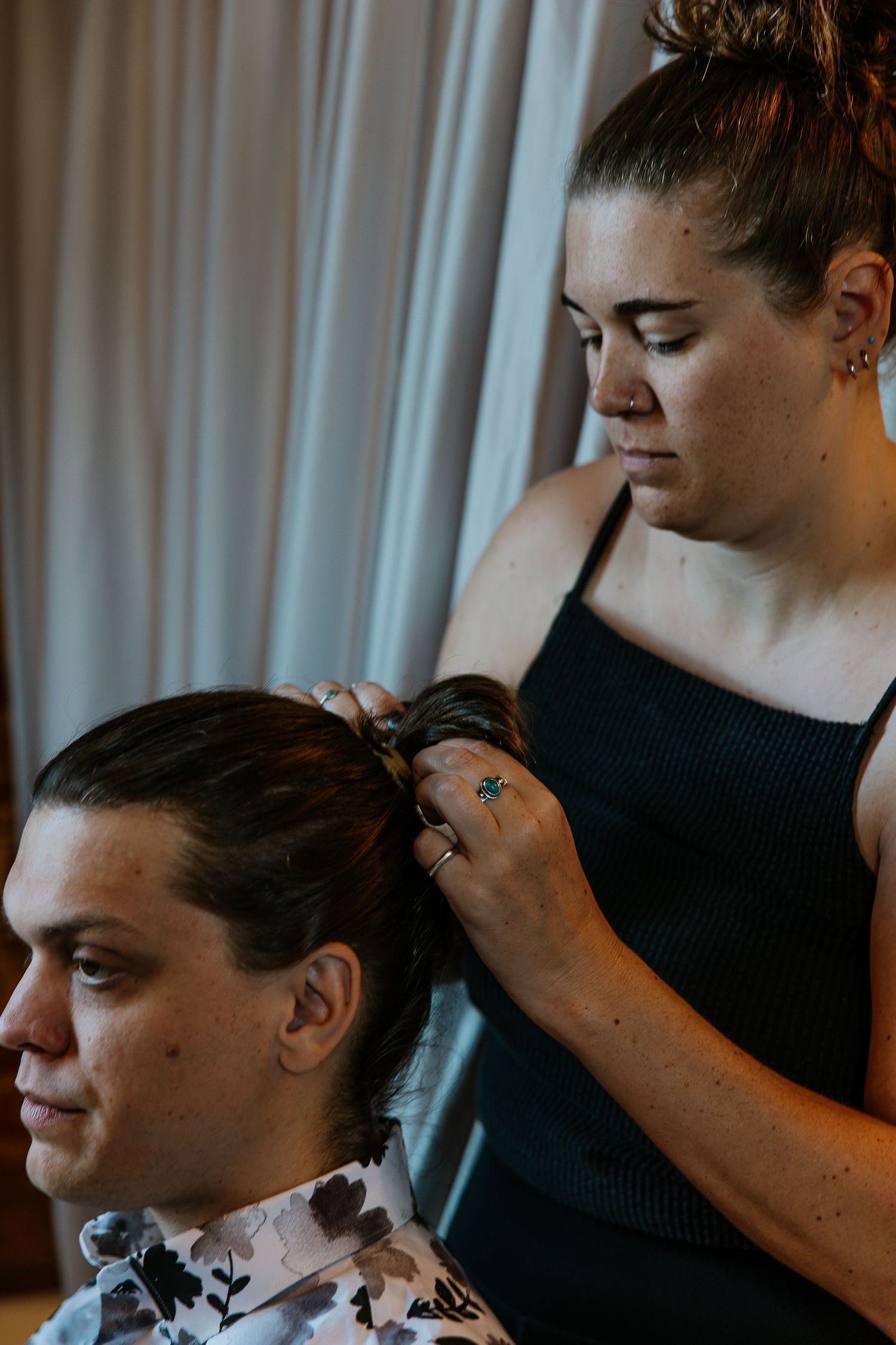 Hair stylist carefully styling a woman's hair in a softly lit room.