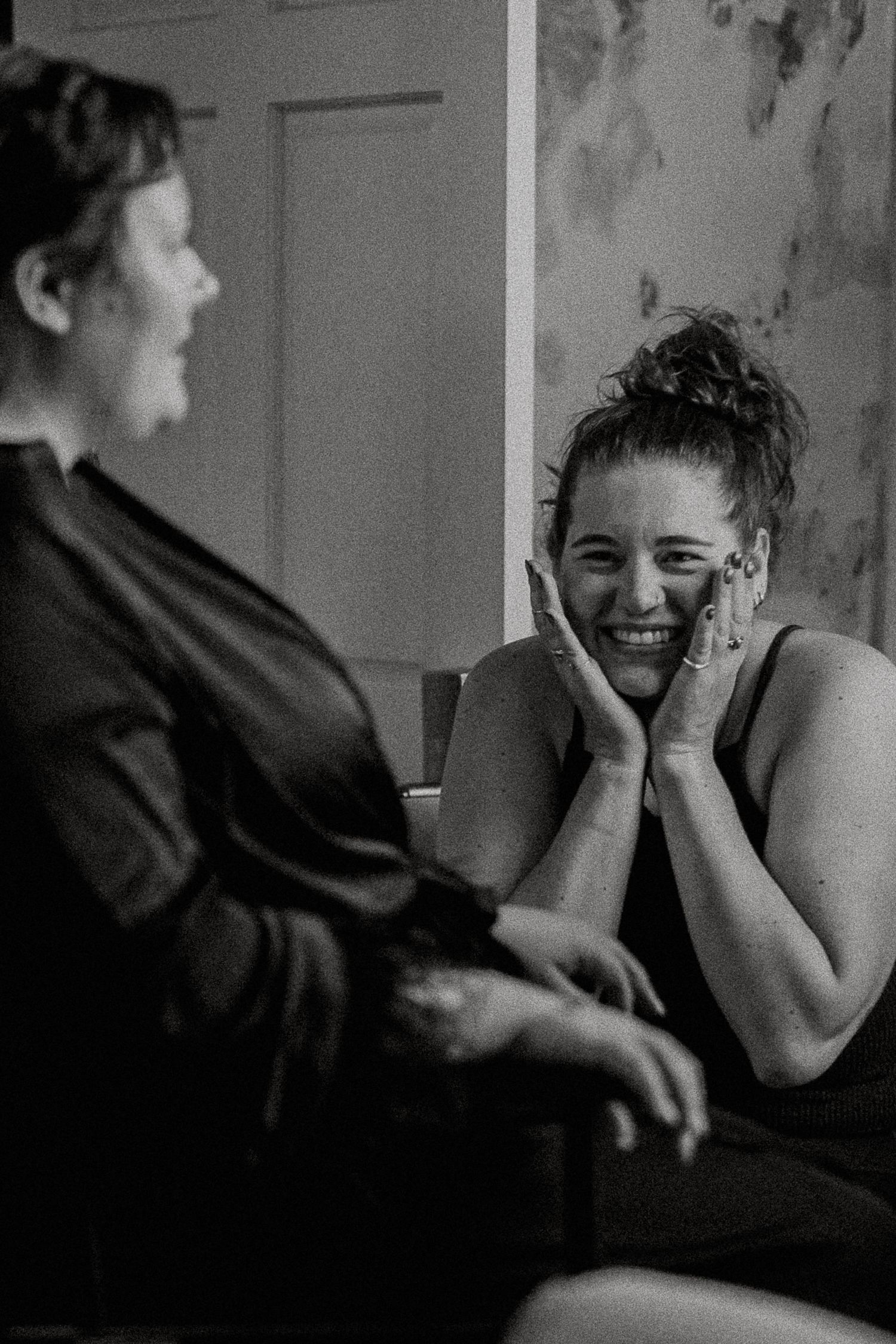 Two women laughing together during wedding preparations in black and white.