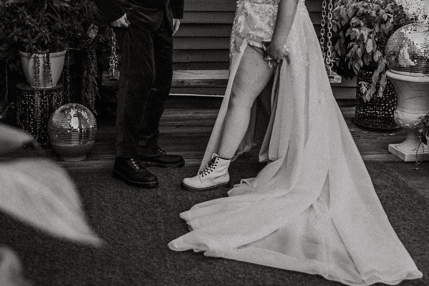 Black and white photo of bride in lace gown wearing white combat boots at wedding ceremony.