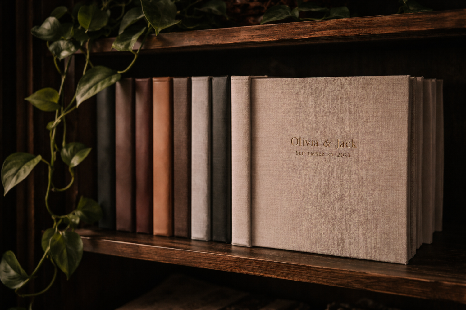 Collection of linen and leather wedding albums displayed on a wooden shelf with ivy plants at Mill Street Studios in Cincinnati, Ohio.