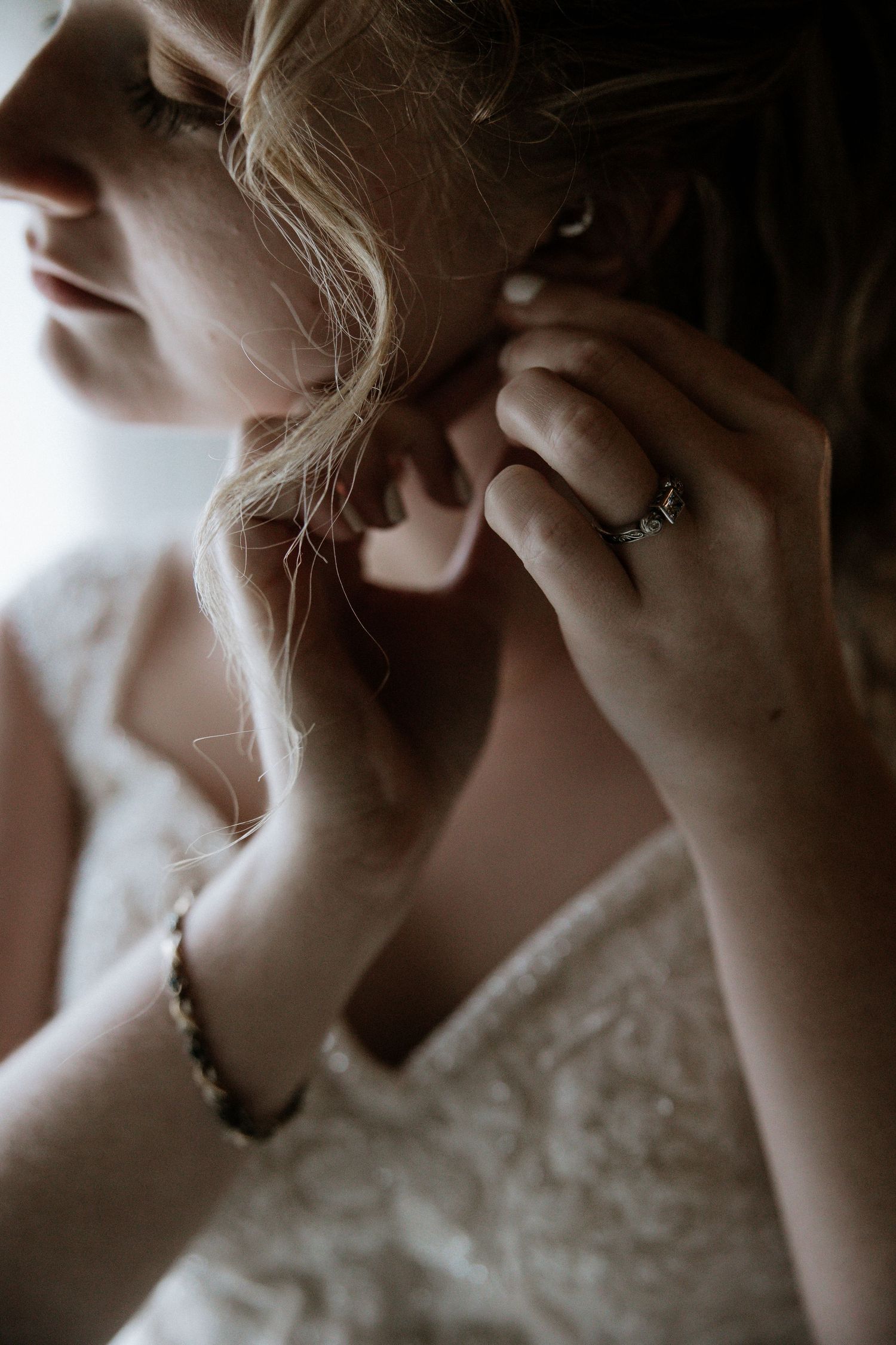 Bride putting on earring while wearing lace wedding dress and diamond engagement ring at The Barn at Wolf Creek in Akron, Ohio
