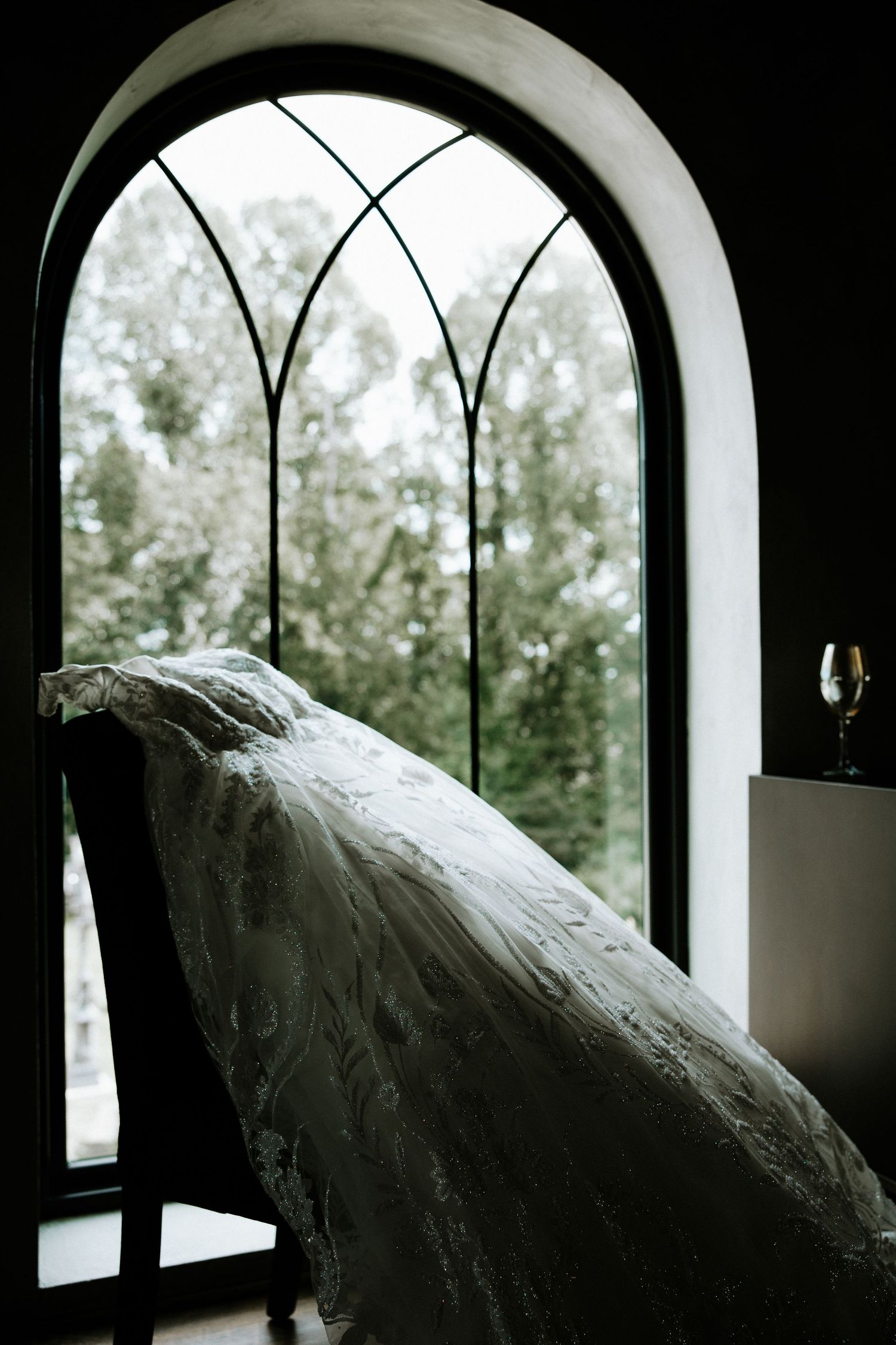 Elegant lace wedding dress draped over a chair near an arched gothic window at the Bella Amore on Enchanted Acres in Dennison, Ohio