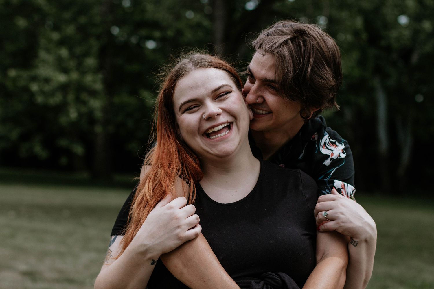 Joyful young couple embracing outdoors, laughing woman with red hair hugged from behind by partner in Dayton, Ohio