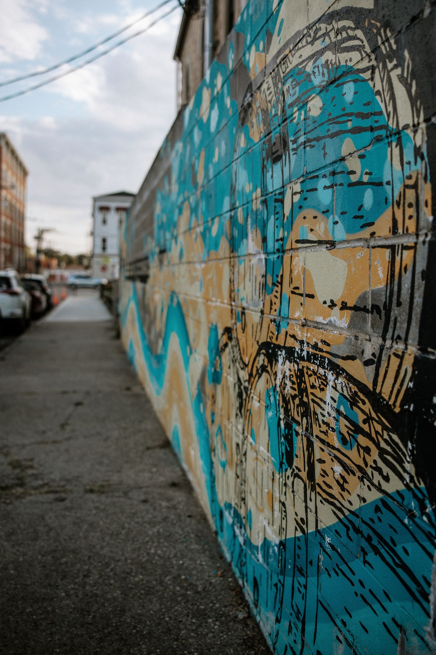 Colorful blue and tan street art mural on a brick building along an urban alleyway at Urban Artifact in Cincinnati, Ohio