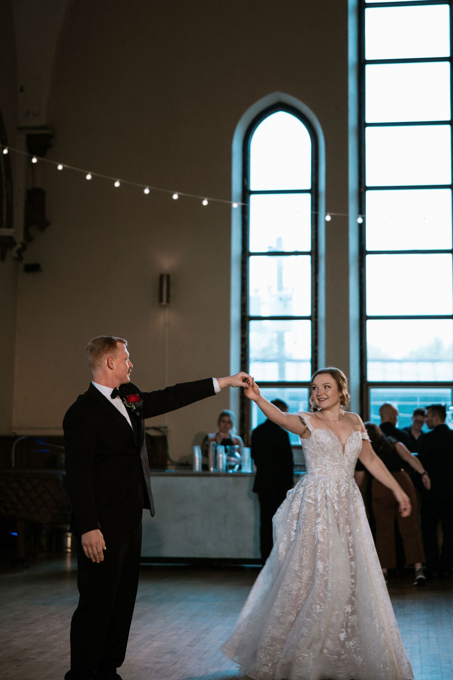 Bride and groom share elegant first dance in grand venue with arched windows and string lights at Urban Artifact in Cincinnati, Ohio