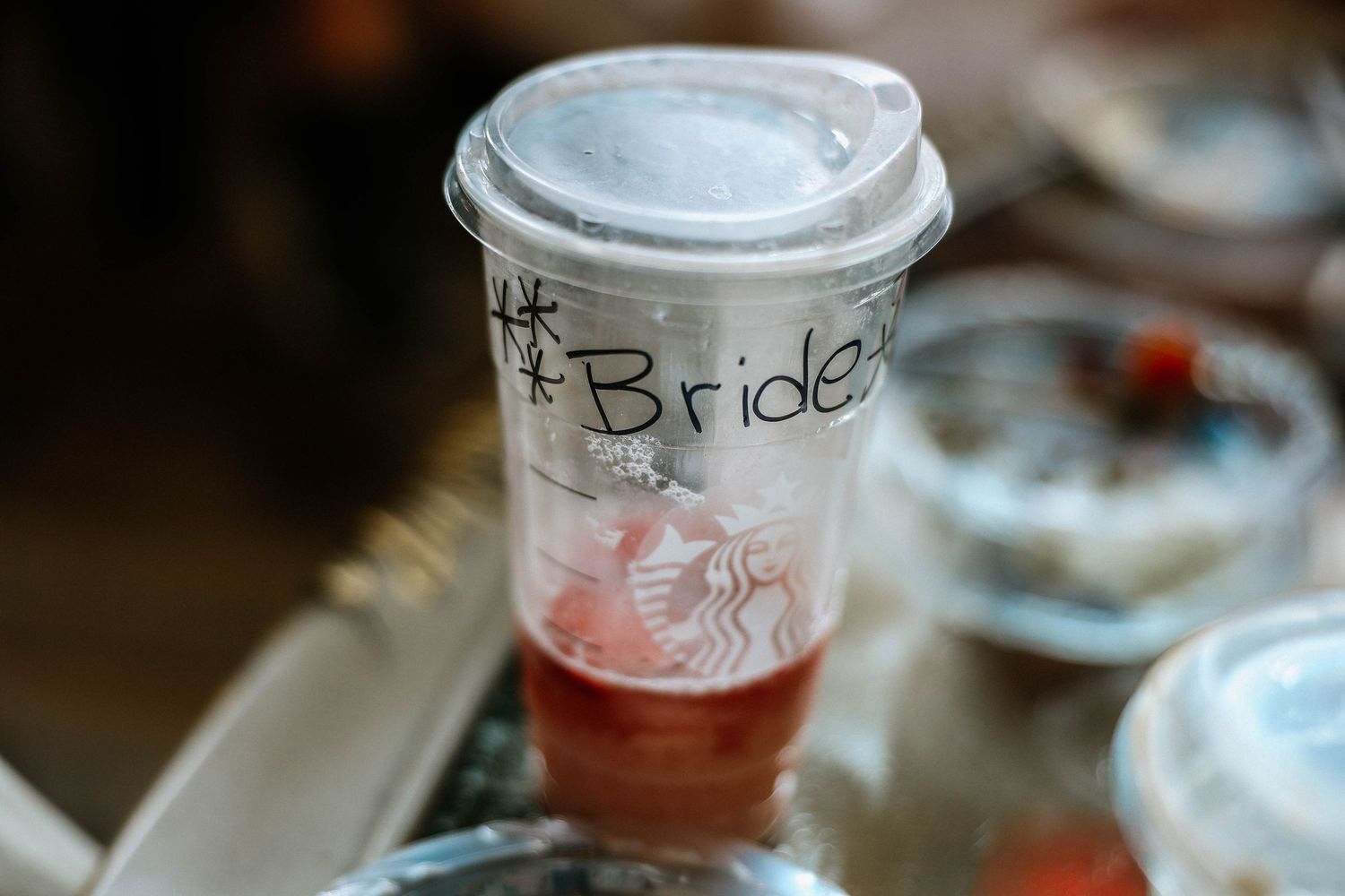 Starbucks cup labeled Bride with red drink inside on table at wedding preparation.