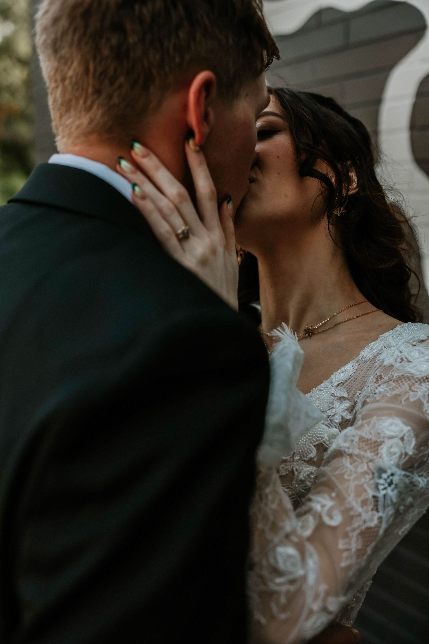 Bride and groom sharing a romantic kiss, bride wearing lace wedding gown and delicate necklace.