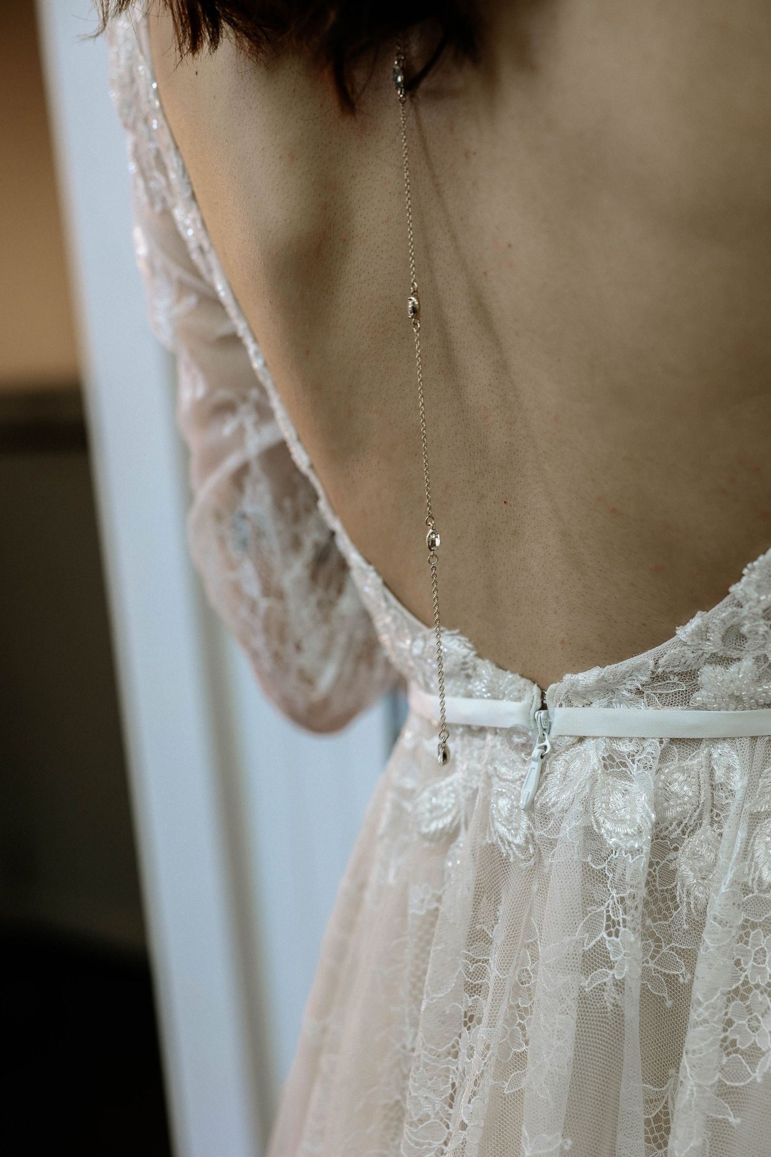 Elegant backless lace wedding dress with a delicate back necklace chain, showcasing intricate floral lace details.