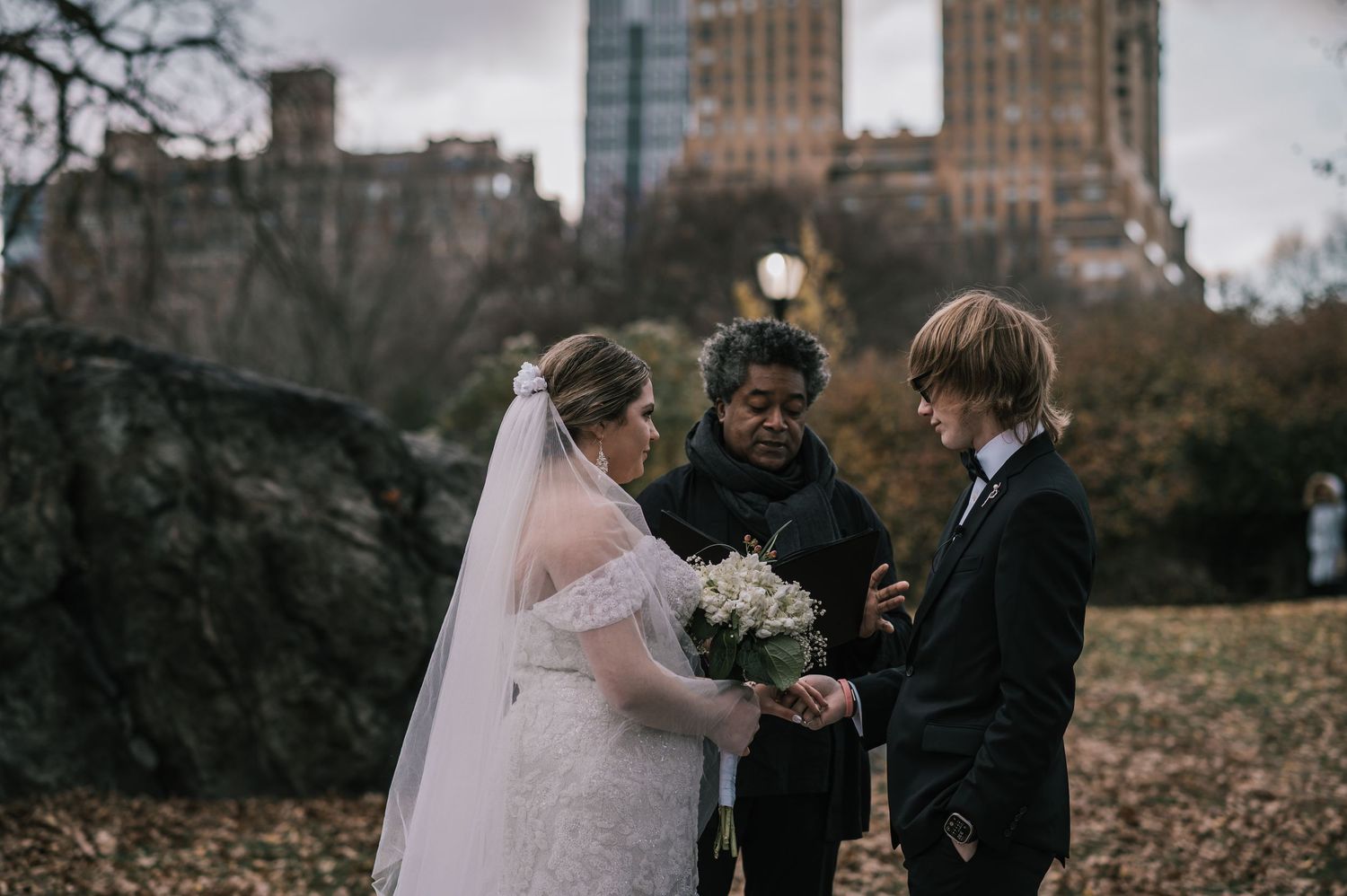Bride and groom holding hands during Central Park wedding ceremony with Manhattan skyline in background.