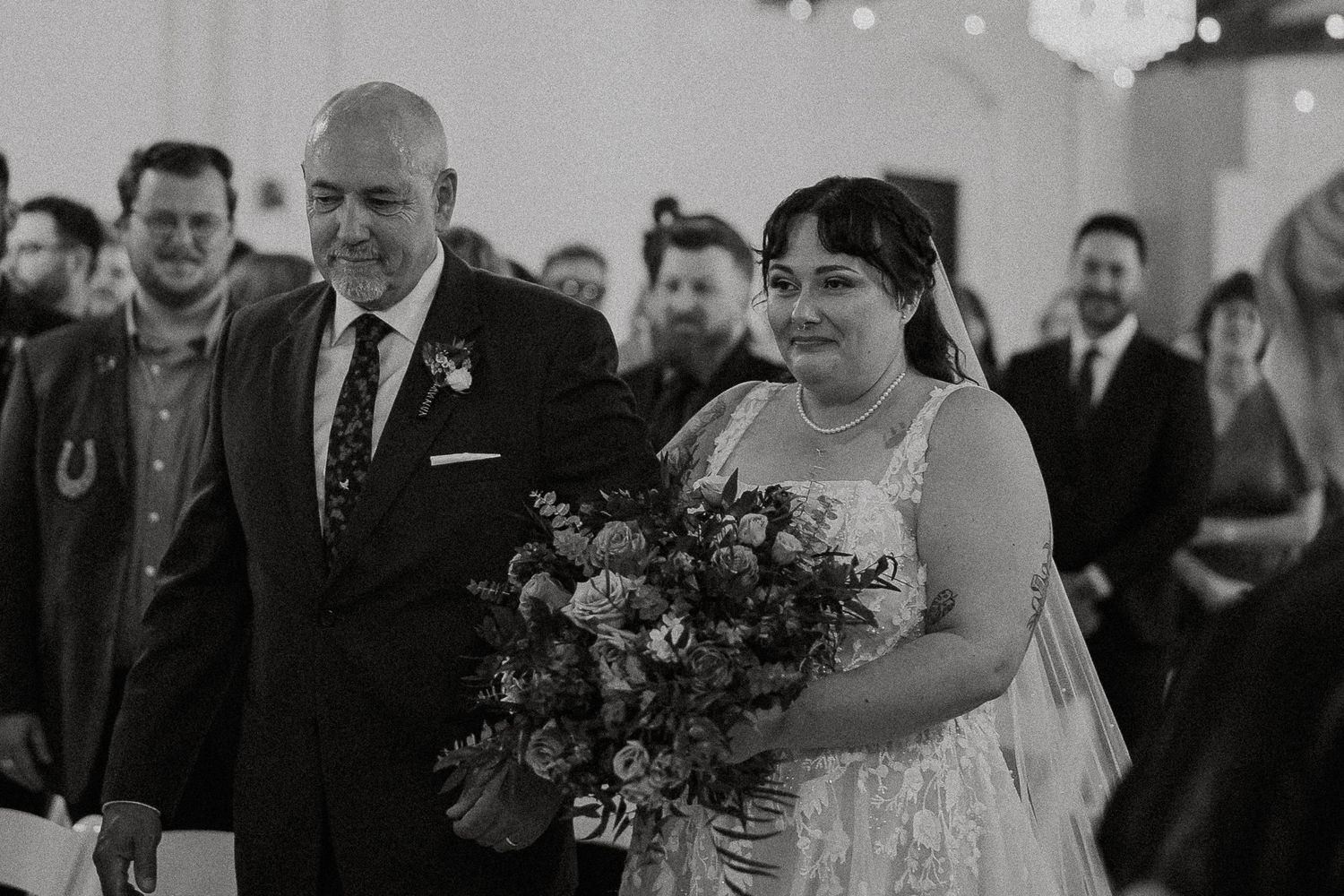 Black and white photo of bride holding bouquet walking down aisle with father.