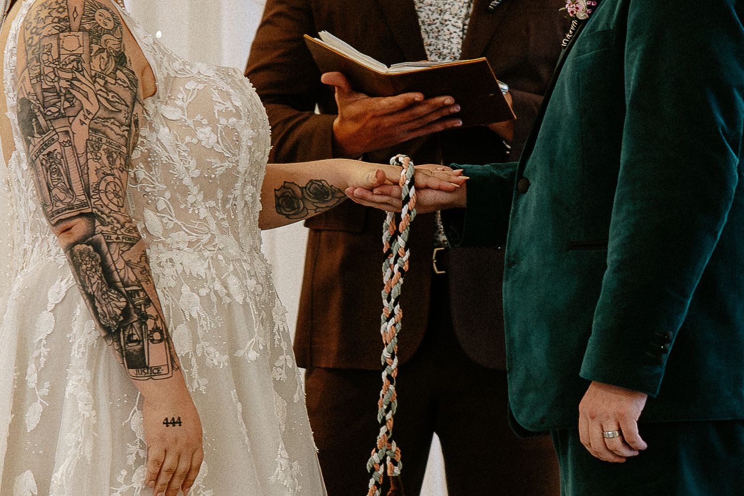 Bride and groom exchange vows during a handfasting ceremony with tattooed arms visible.