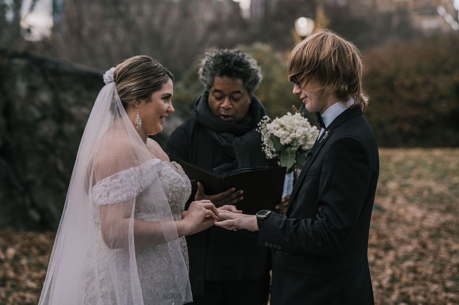 Close-up of bride placing ring on groom's finger during intimate Central Park wedding ceremony in fall.