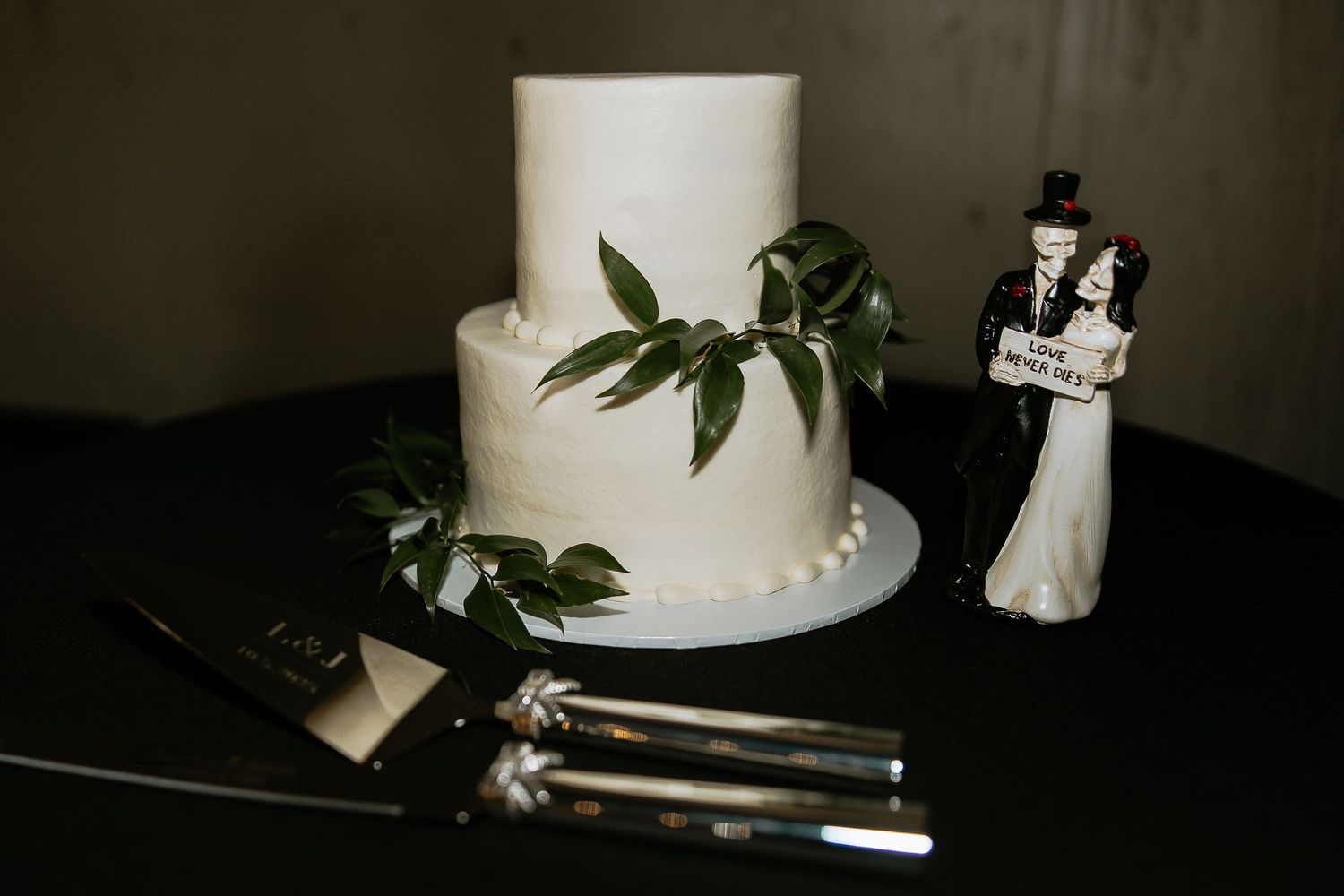 Simple two-tier white wedding cake with greenery accents and classic bride and groom cake topper.