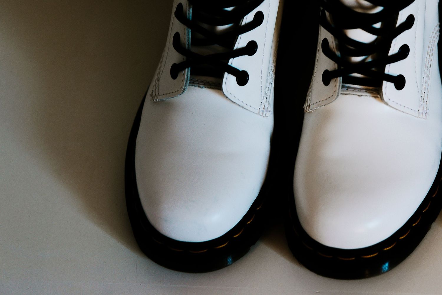 White Dr. Martens boots with black laces on a neutral background.