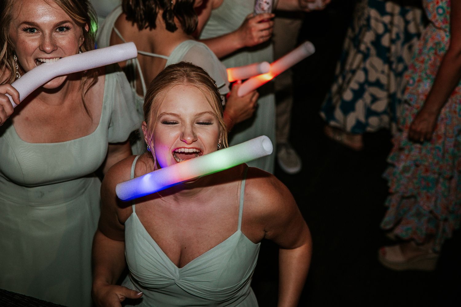 Bridesmaid dancing joyfully with colorful glow sticks at lively wedding reception party.