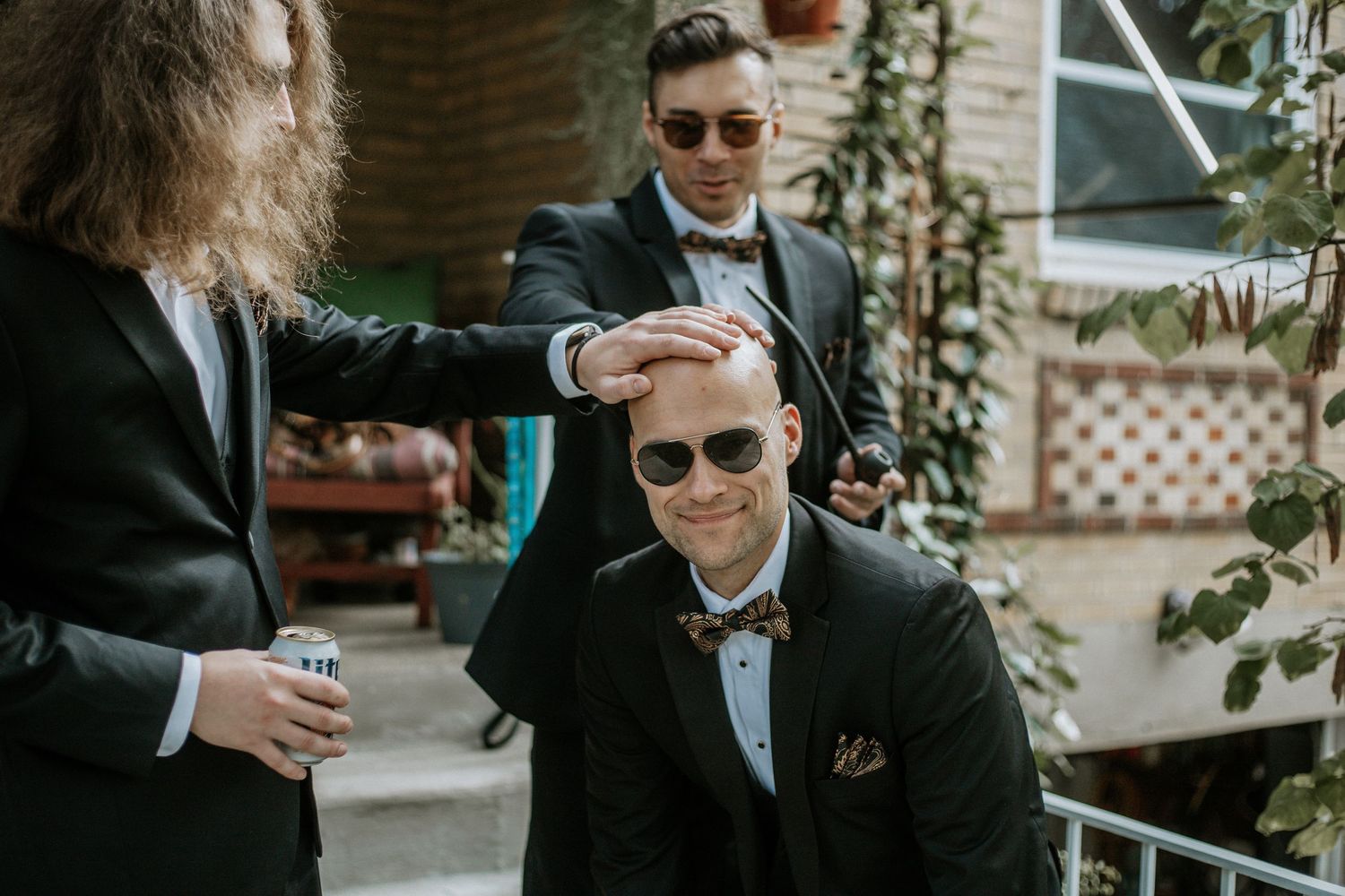 Groomsmen in black tuxedos playfully style the groom's hair outdoors before the wedding ceremony in Cincinnati, Ohio