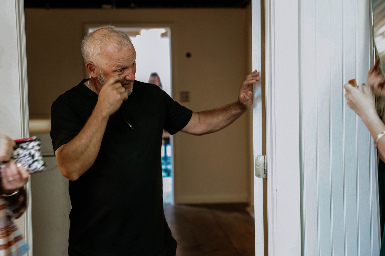 Emotional elderly man covering his mouth in surprise while standing in a doorway during a heartfelt moment.