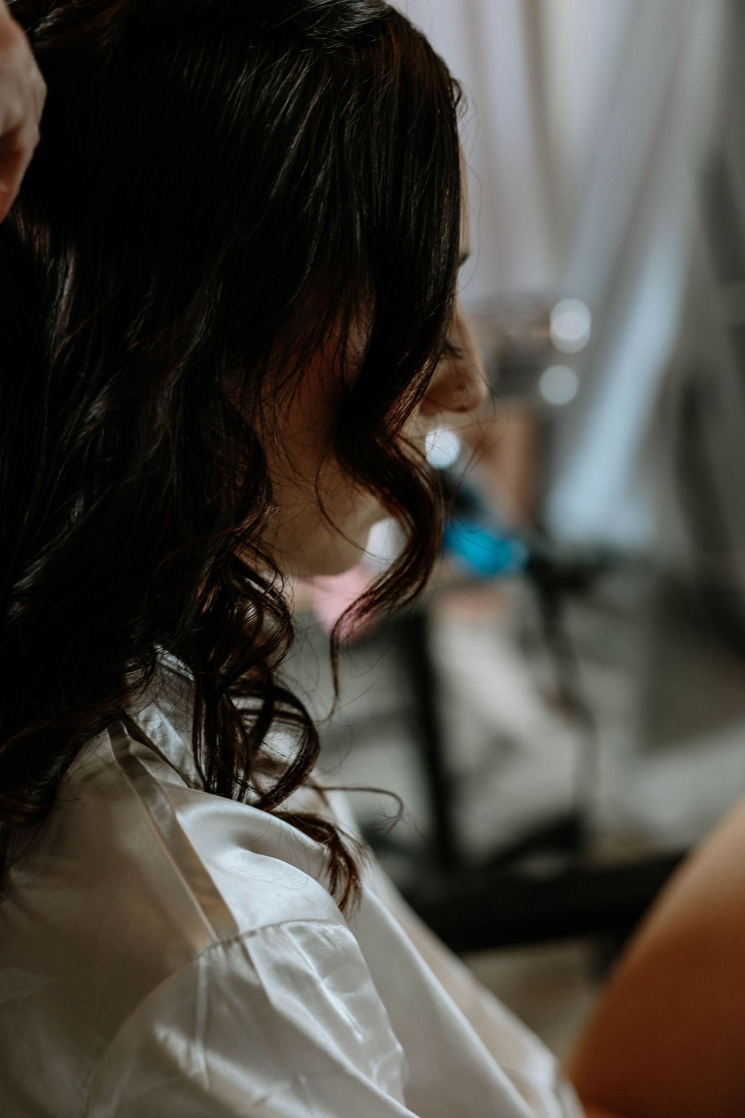 Close-up of bride with beautiful dark curly hair wearing a white robe during wedding preparation.