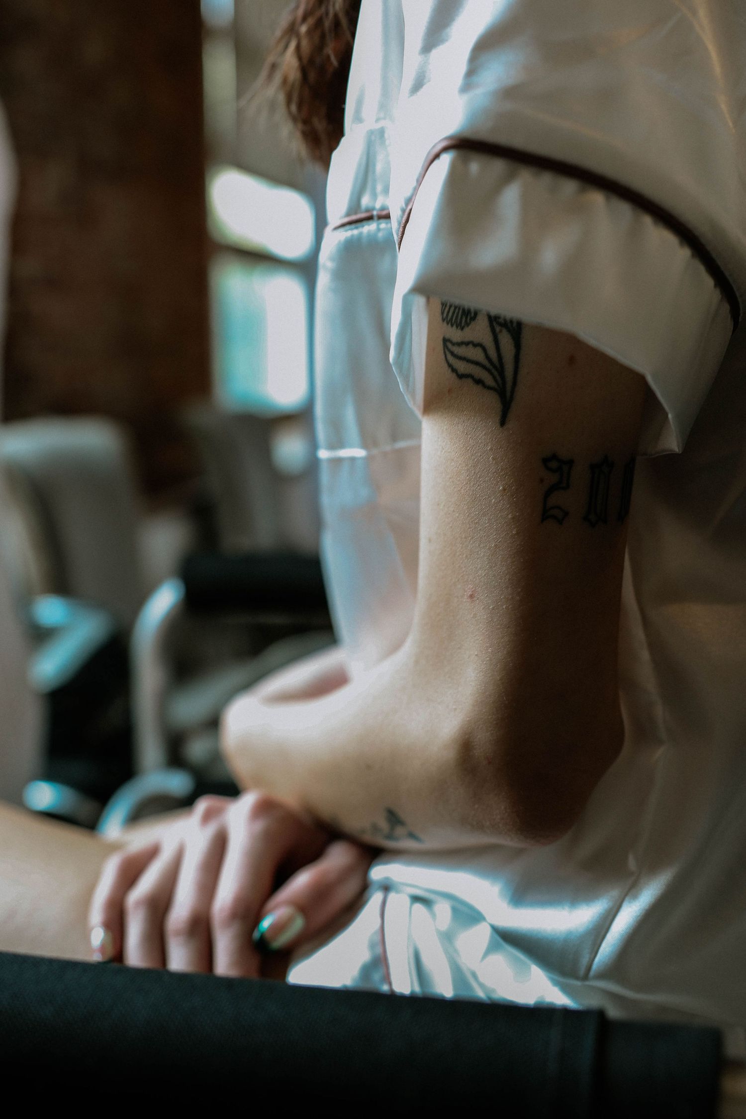 Close-up of a person in white shirt showing arm tattoos including a floral and text design.