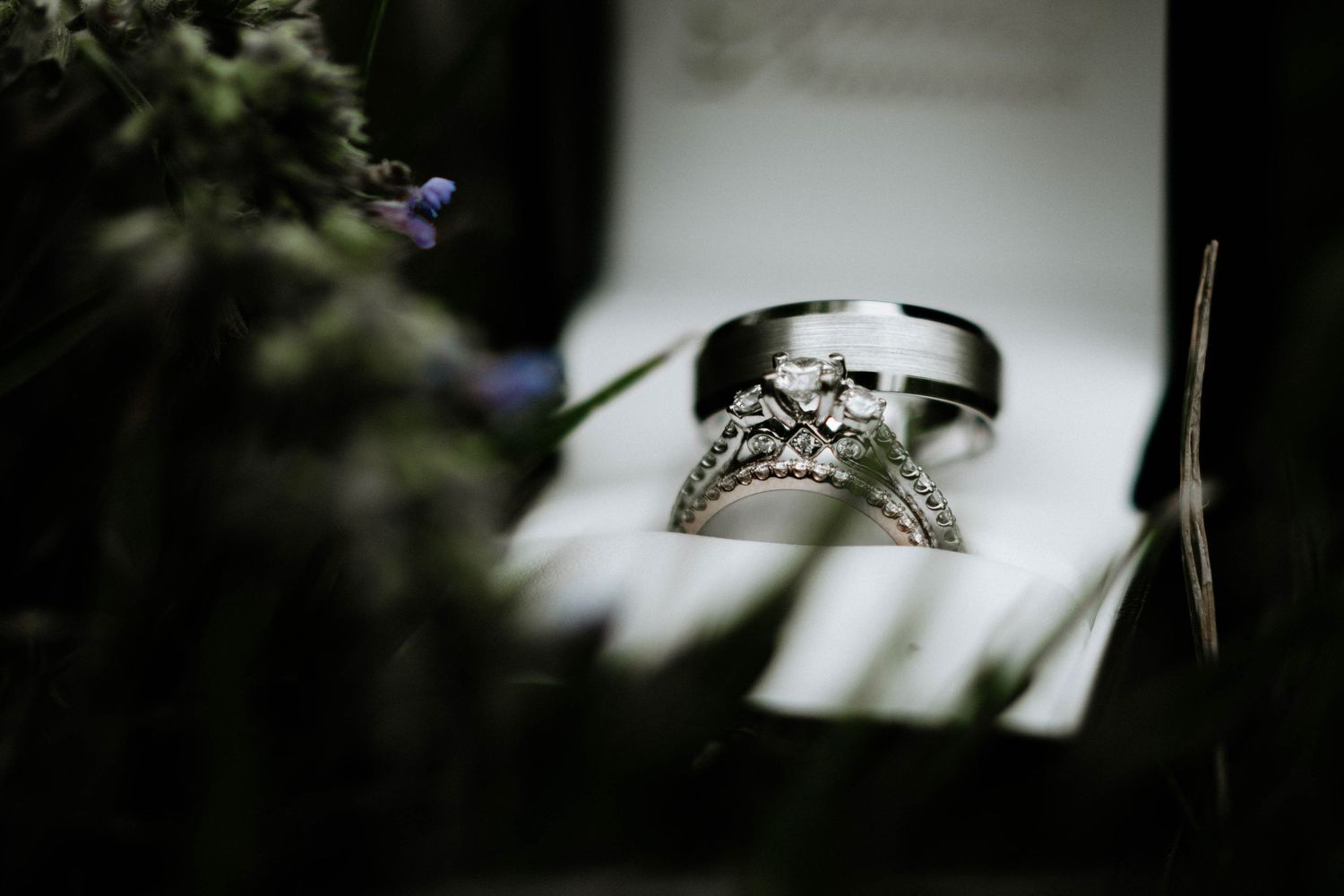 Elegant diamond engagement ring and wedding band displayed in white jewelry box with floral background.