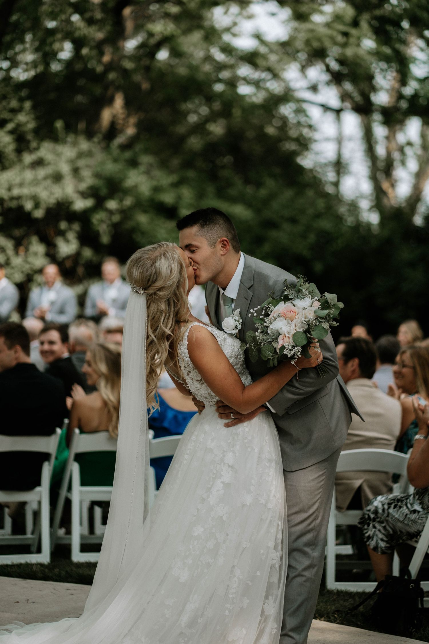 Bride and groom share first kiss at outdoor wedding ceremony with guests seated nearby at Stone Valley Meadows in Dayton, Ohio