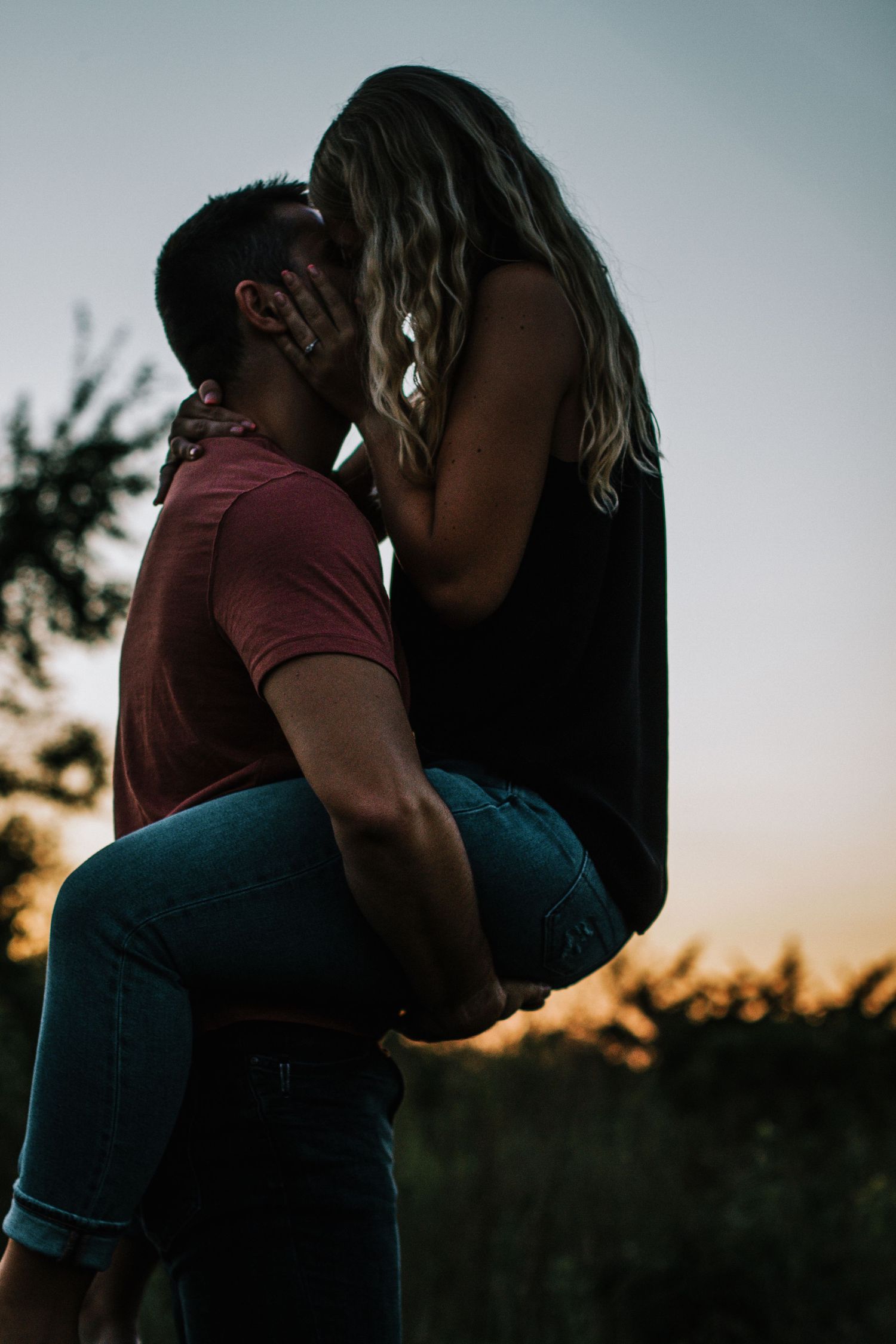 A romantic couple shares a passionate kiss at sunset, the man lifting the woman in his arms outdoors in Cincinnati, Ohio