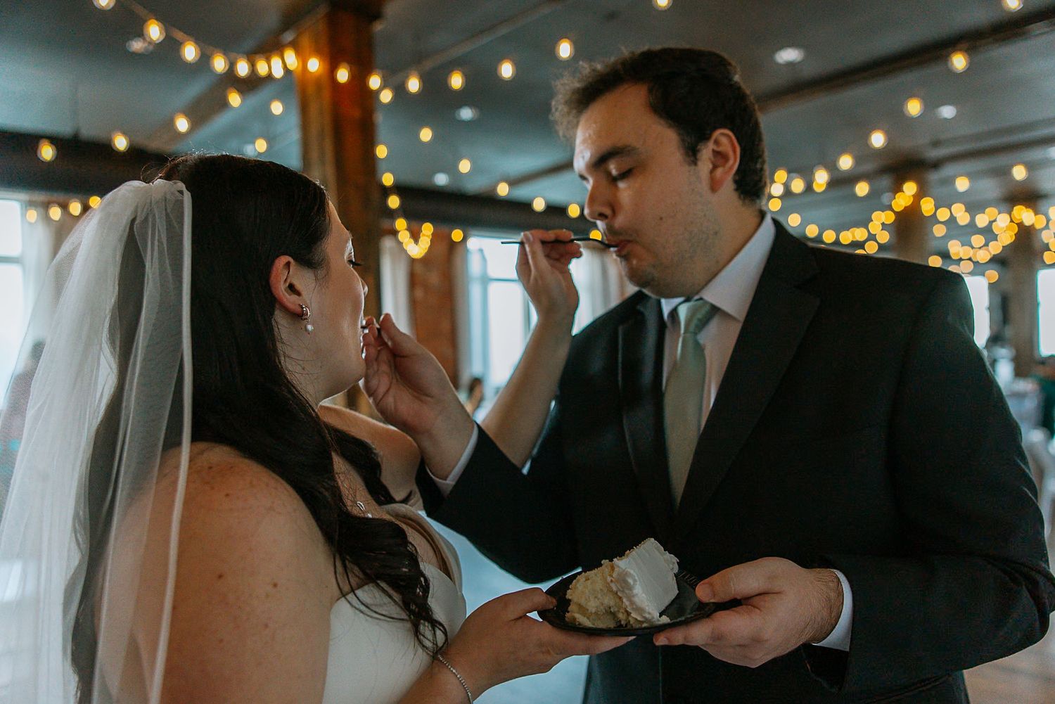 Bride feeds groom a bite of wedding cake during the cake cutting ceremony at reception.