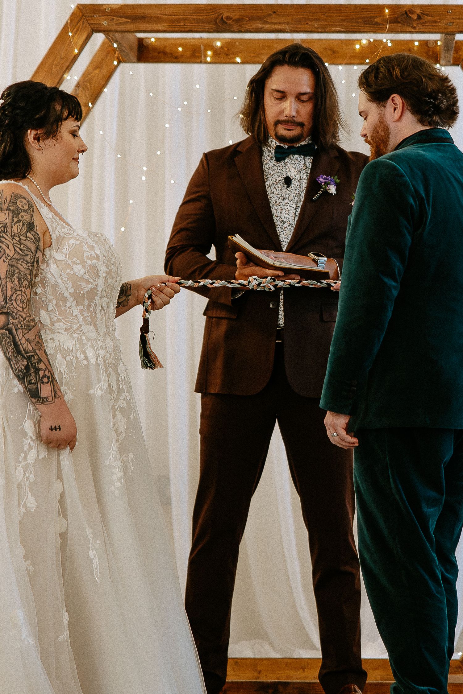 Officiant holding ceremonial tray as tattooed bride and groom perform handfasting ritual.