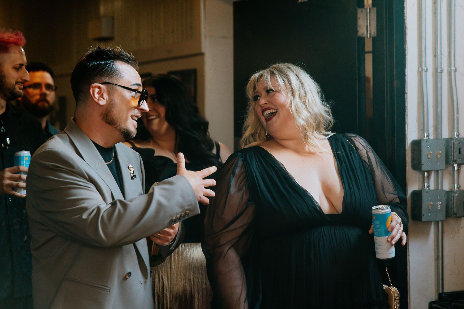 Two guests laughing together at wedding reception, man in gray suit and woman in black gown.