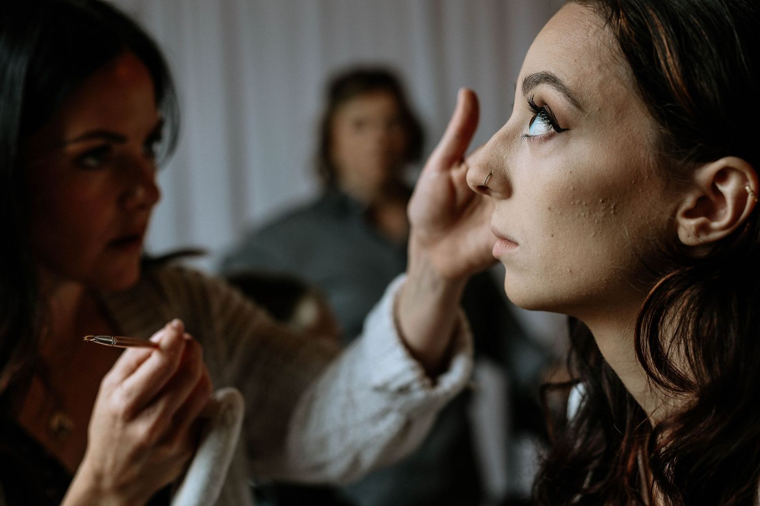 A makeup artist applies cosmetics to a young woman's face during bridal preparation at an indoor venue.