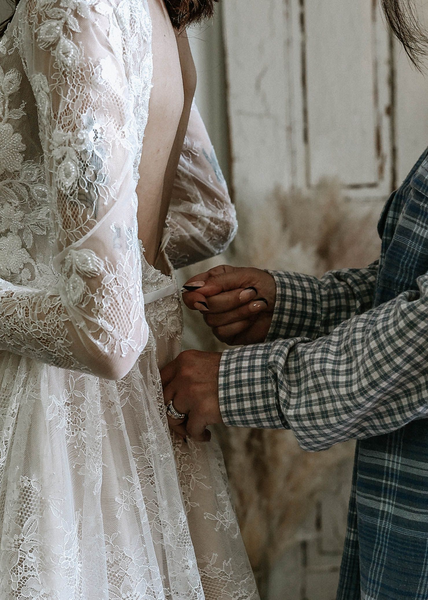 Person fastening the back of a lace wedding dress on a bride wearing long sleeves.