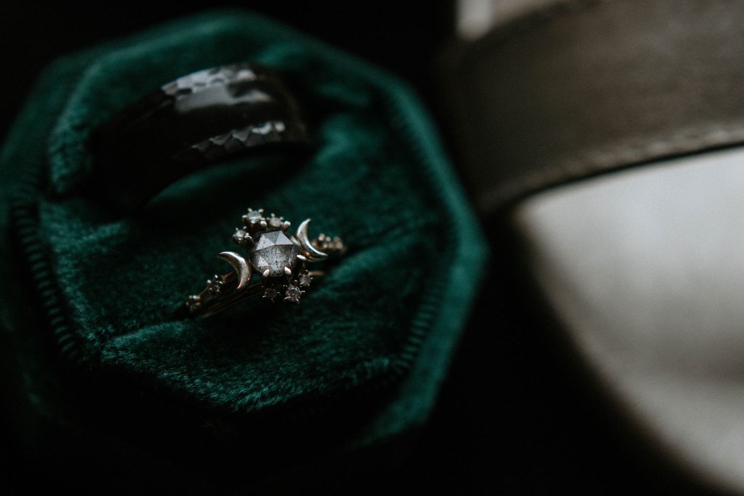 Celestial crescent moon diamond engagement ring and black wedding band in a green velvet ring box.
