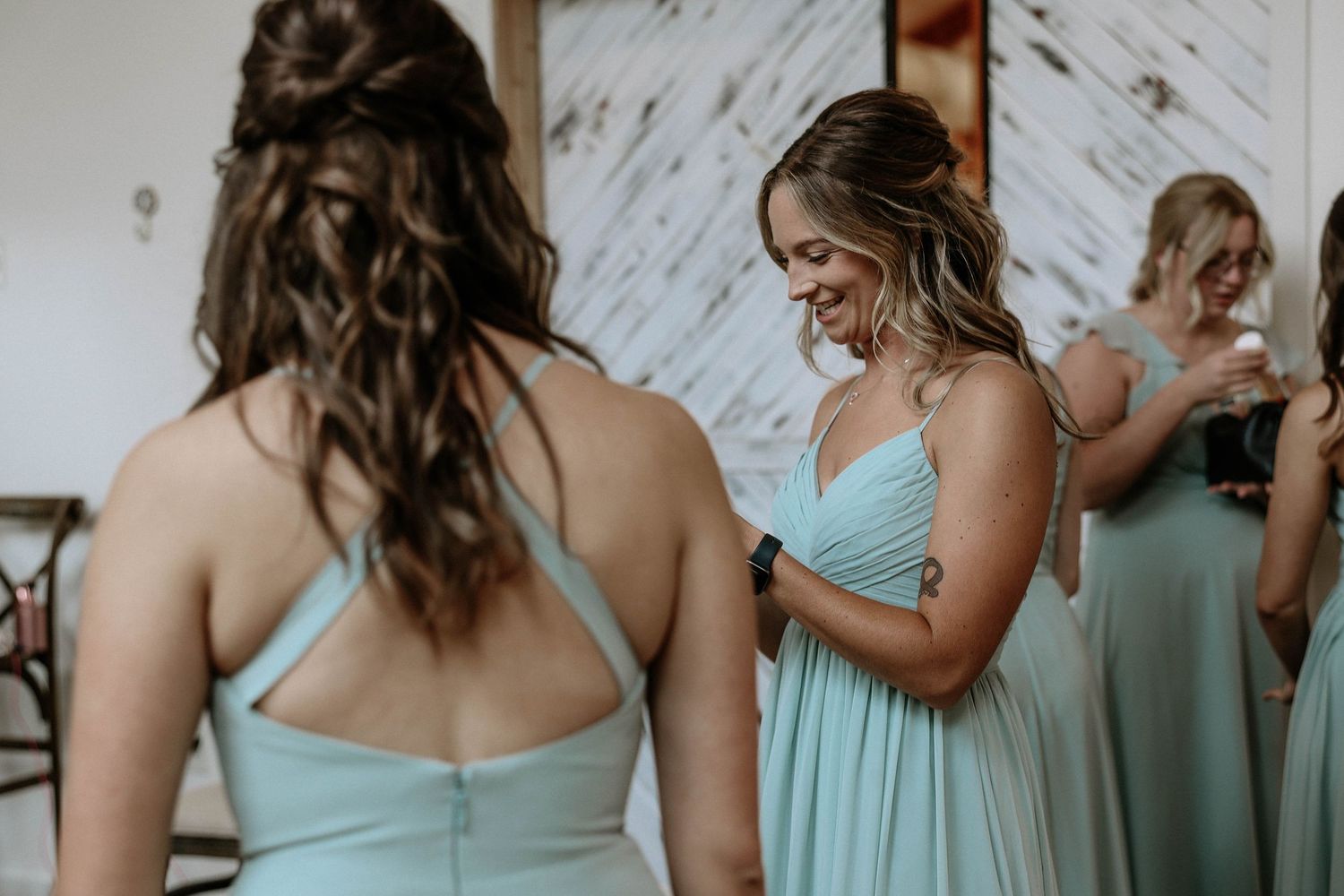 Bridesmaids in mint green dresses helping each other get ready before the wedding ceremony.