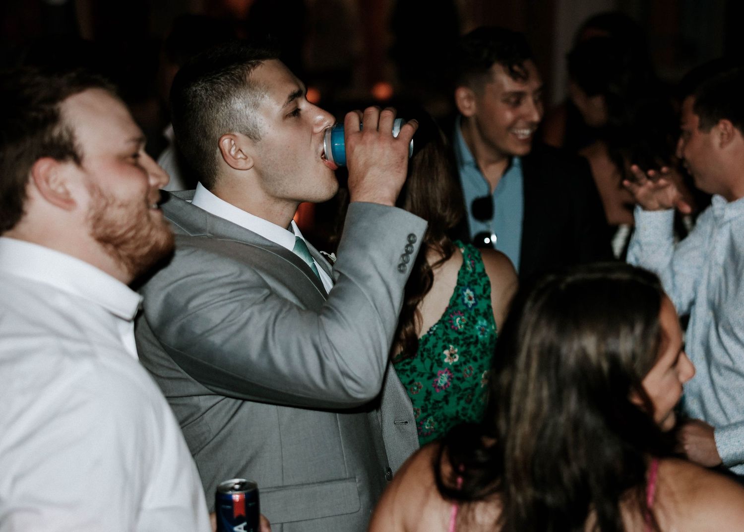 Man in gray suit drinking at a lively wedding reception dance floor party.