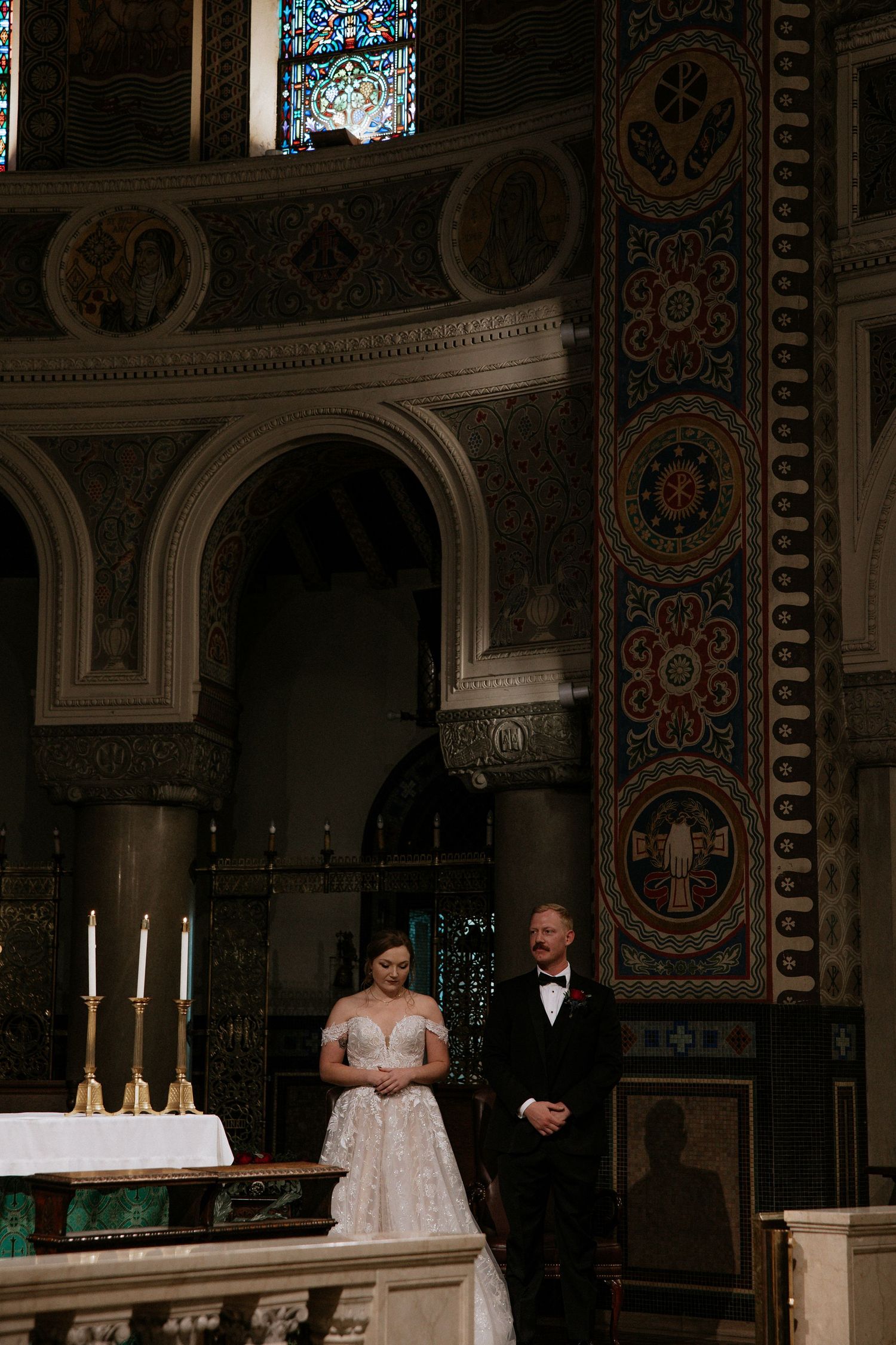 Bride in white gown stands with officiant at ornate church altar with candles and decorative columns in Cincinnati, Ohio
