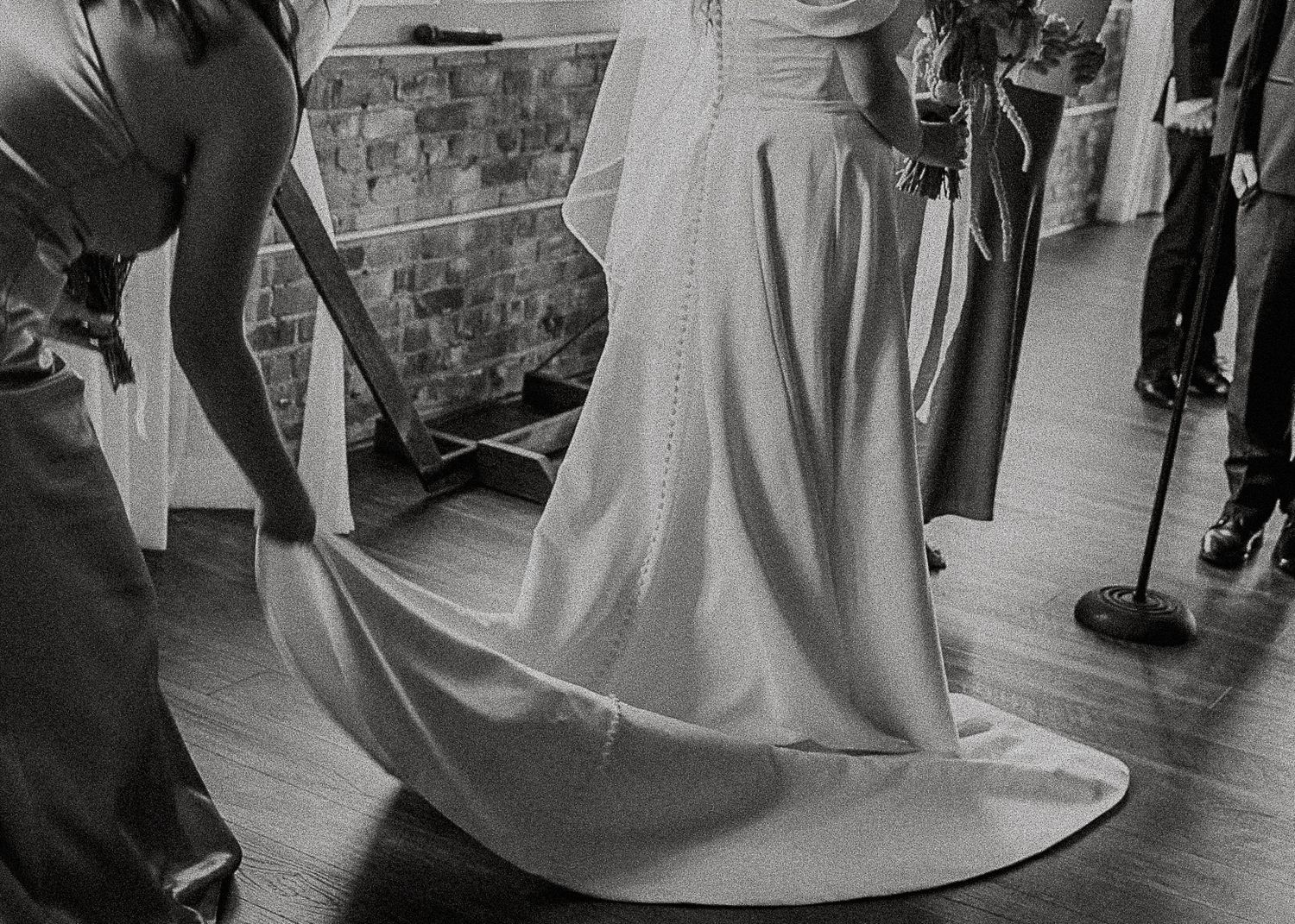Black and white photo of bridesmaids arranging bride's wedding gown train before ceremony.