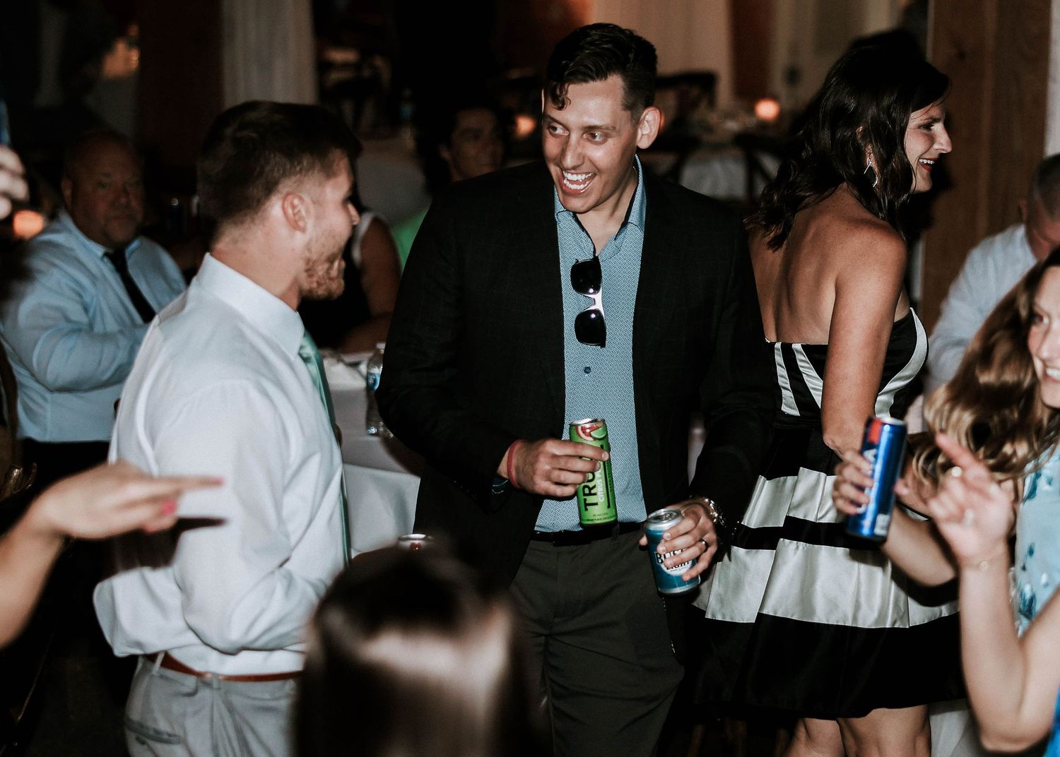 Smiling man in black blazer enjoying drinks with guests at wedding reception.
