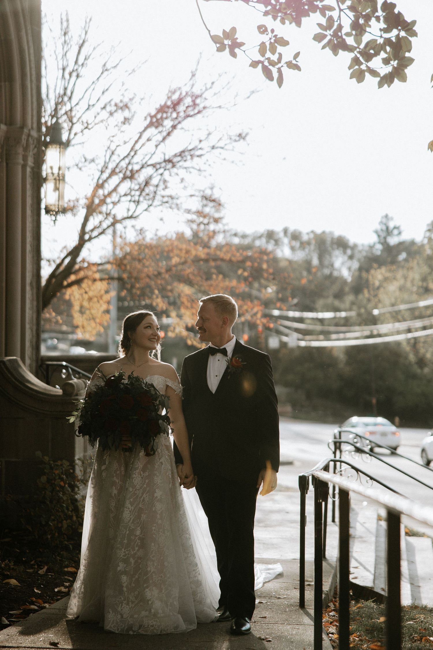 Bride and groom holding hands walking outside historic building in autumn wedding portrait.
