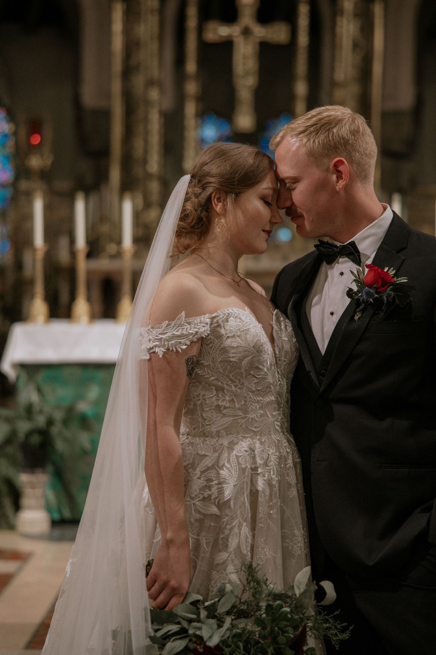 Bride and groom share a tender forehead touch in a beautiful church, bride holding red floral bouquet in Cincinnati, Ohio
