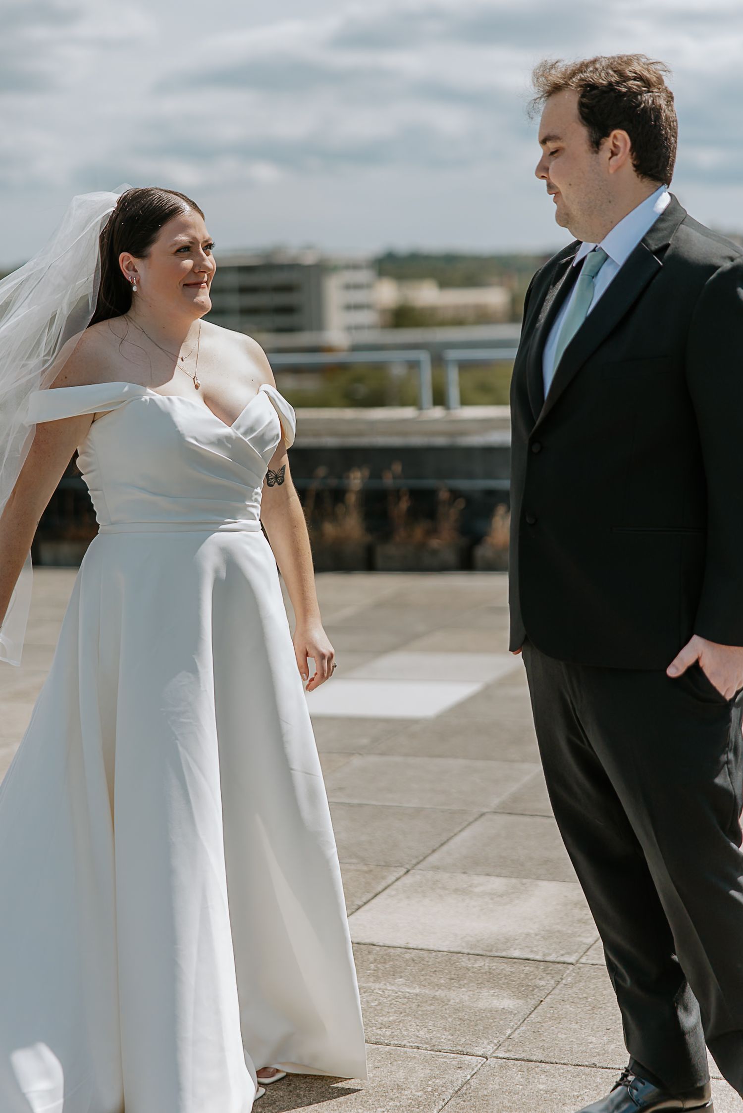 Bride and groom smiling at each other on a rooftop terrace with city buildings behind them.