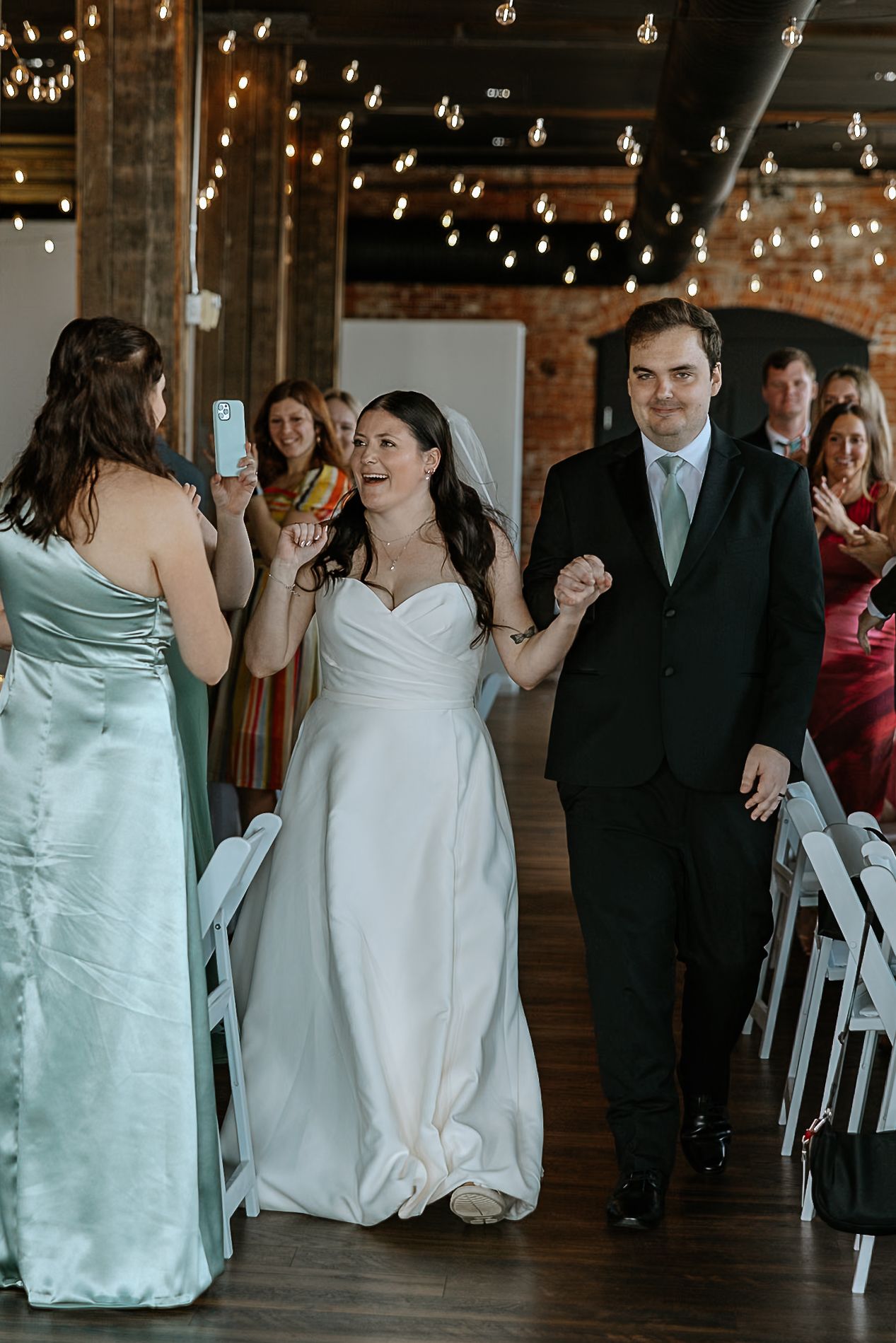 Smiling bride in white gown and groom in dark suit walk down the aisle after wedding ceremony.