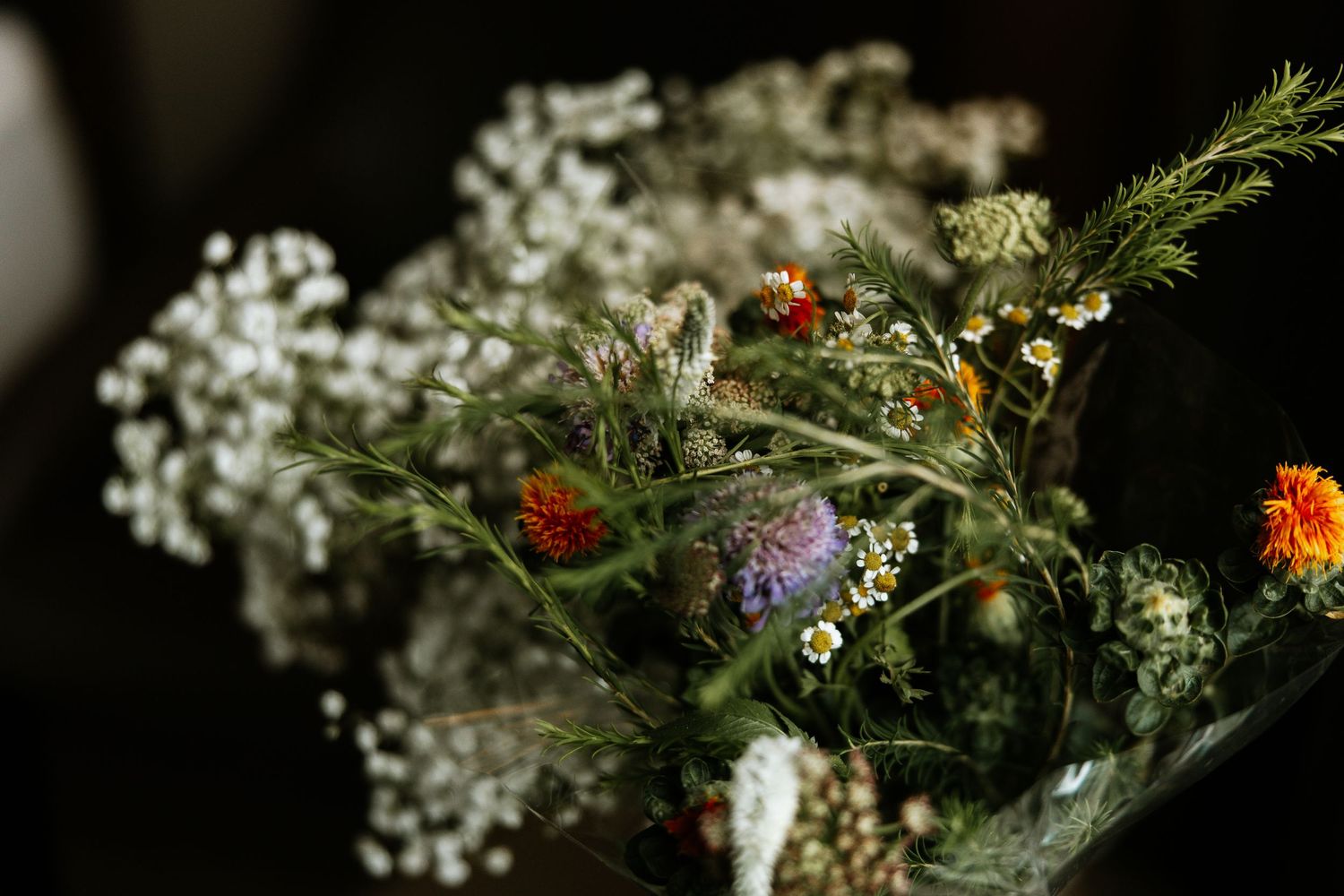 Close-up of rustic wildflower wedding bouquet with orange, white, and purple blooms.