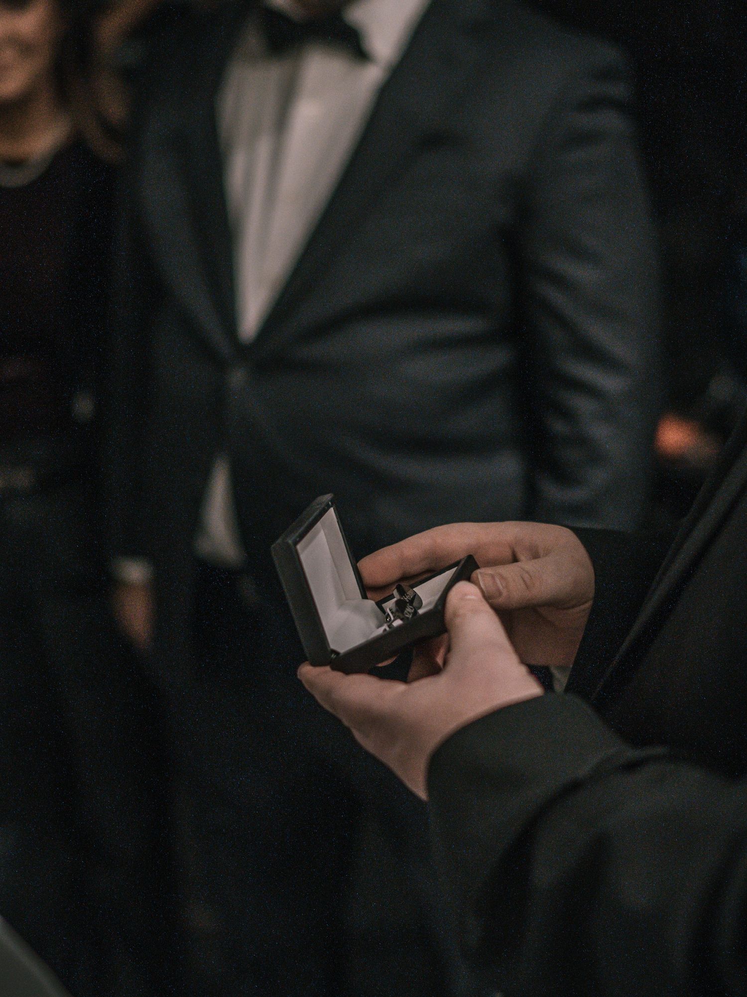 Close-up of hands holding open ring box with wedding band at elegant formal ceremony.
