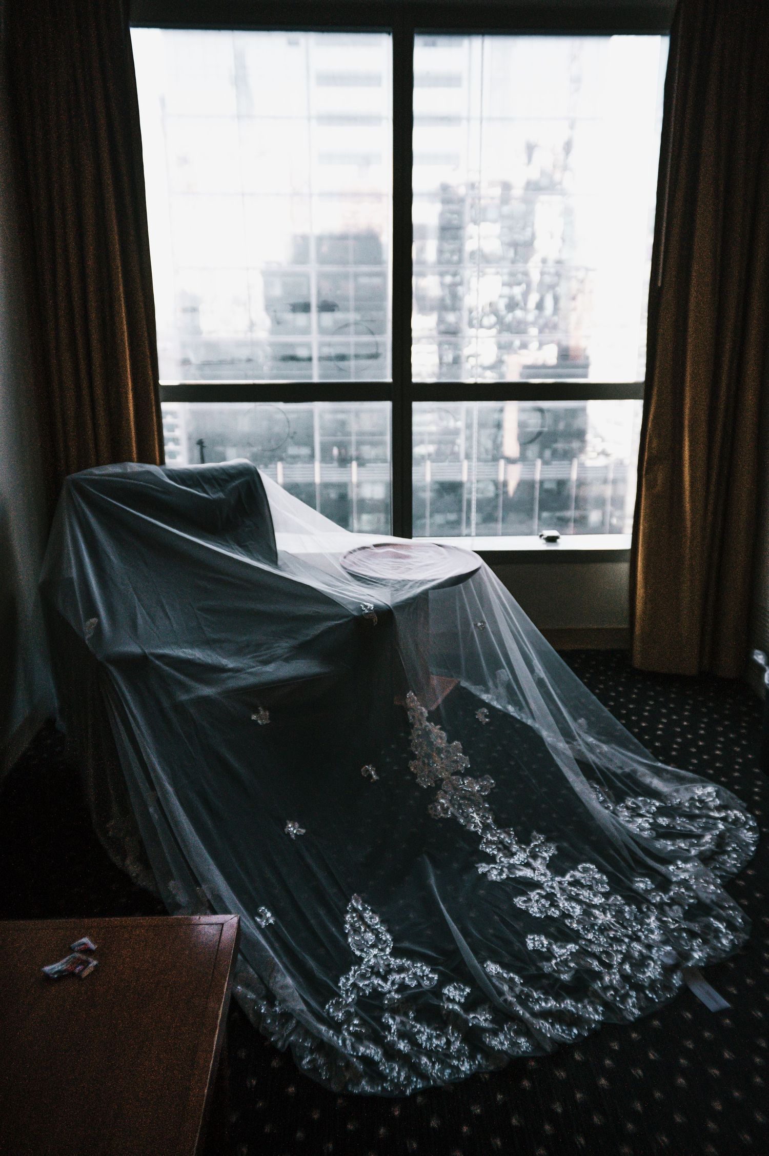 Embroidered cathedral wedding veil draped over chair near hotel window.