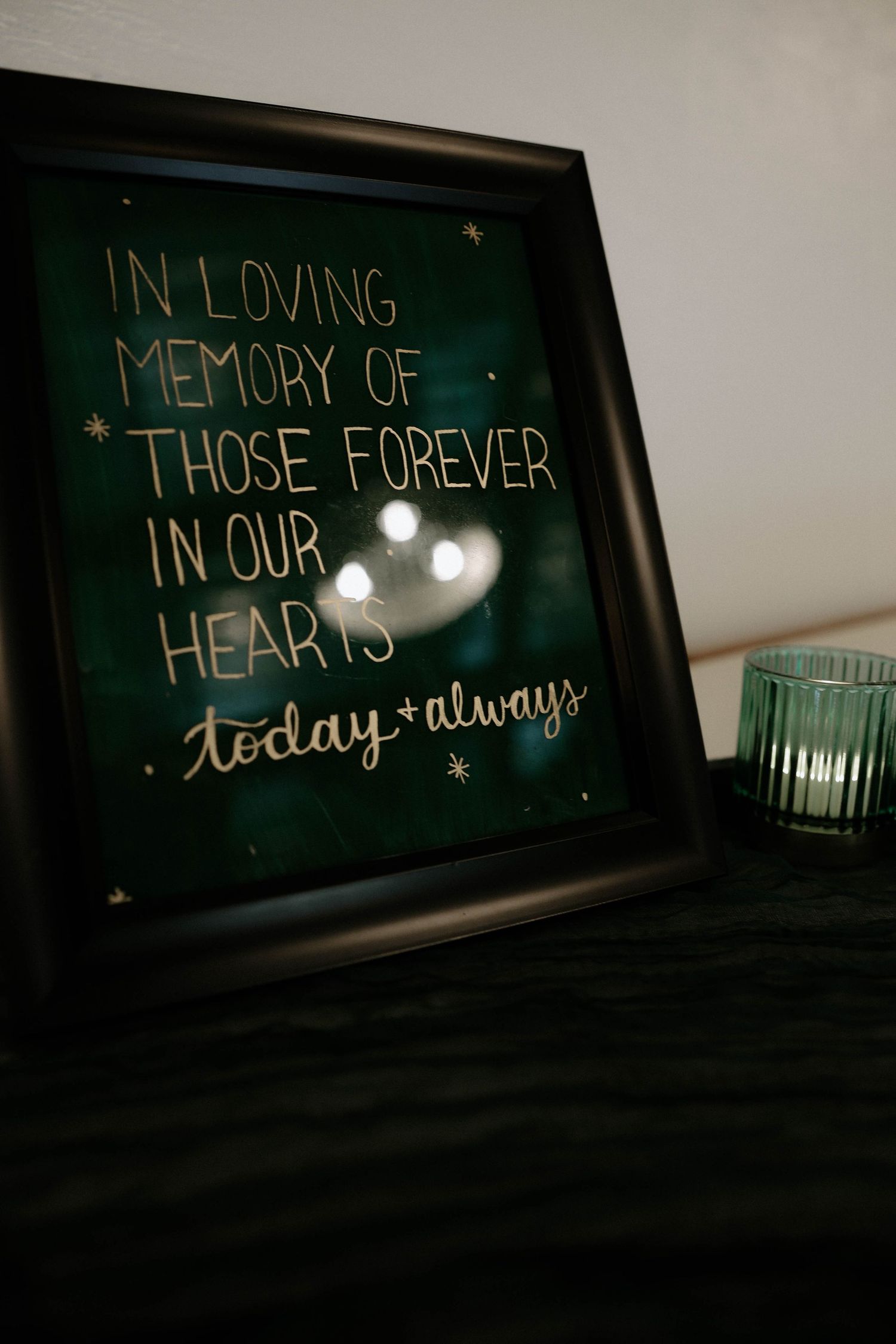 Framed memorial sign reading 'In Loving Memory of Those Forever in Our Hearts today and always' on dark fabric.