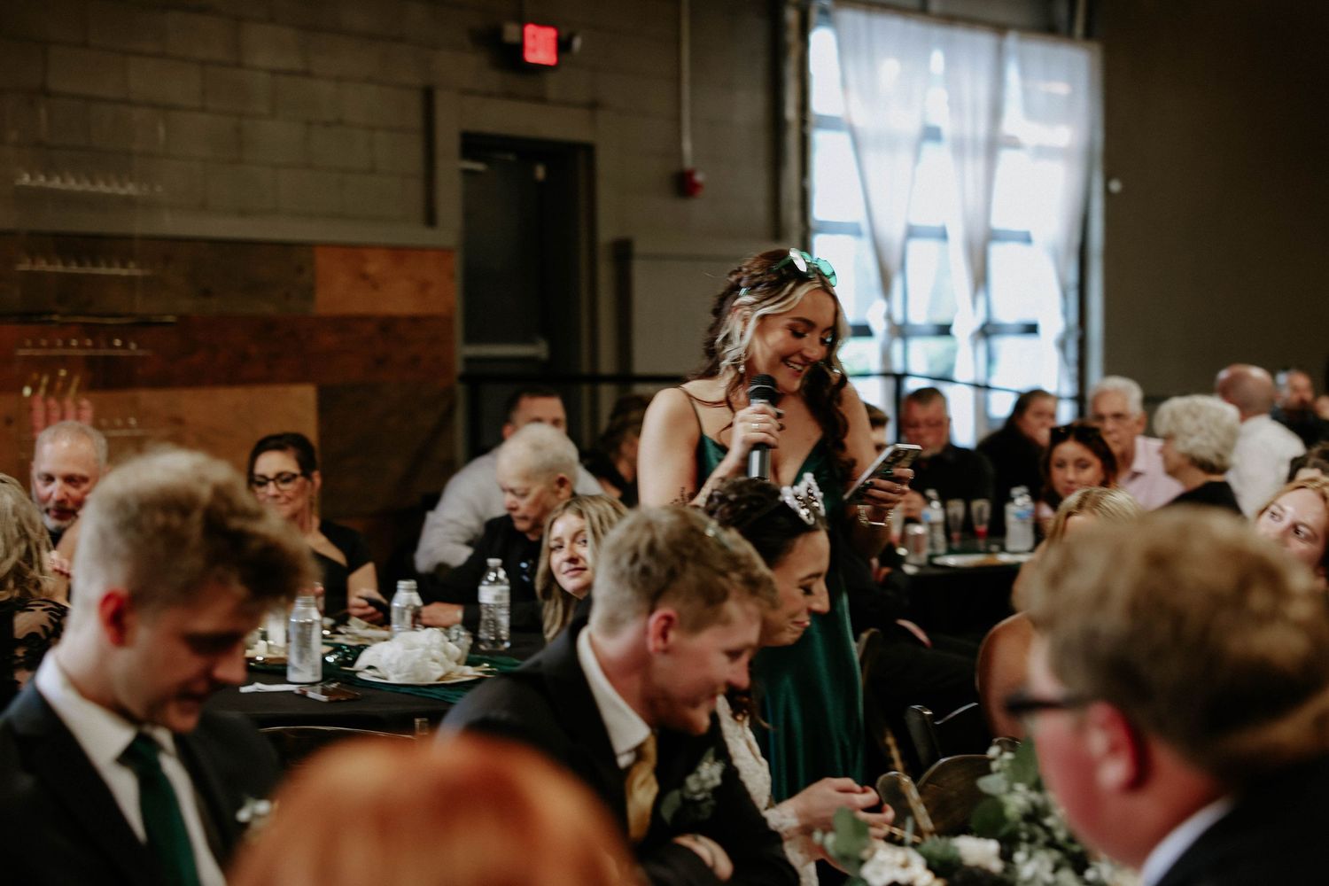 Woman giving a speech with microphone at an elegant wedding reception in an industrial venue.