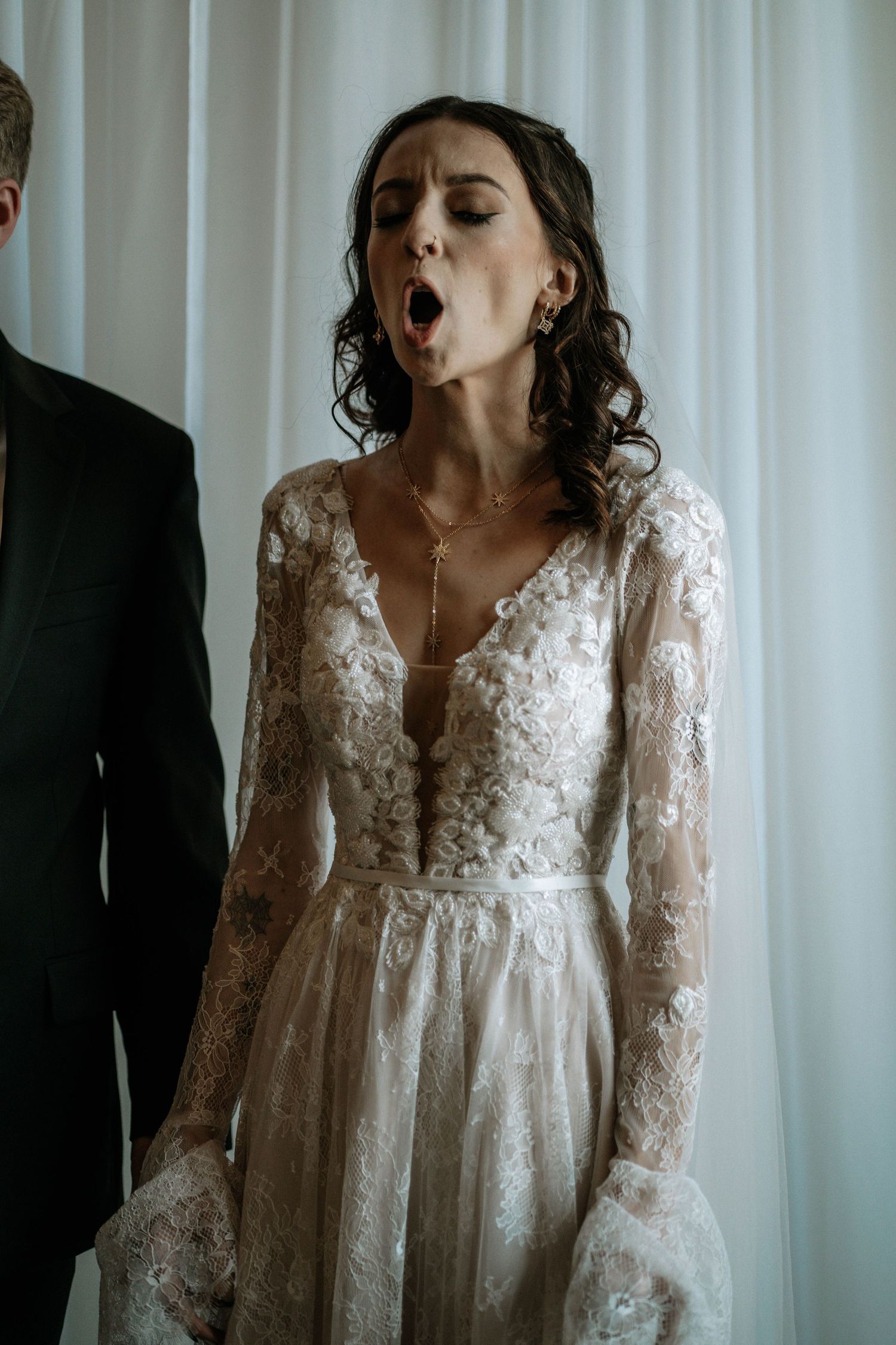 Beautiful bride in elegant long-sleeve lace wedding dress with floral details and delicate gold jewelry.