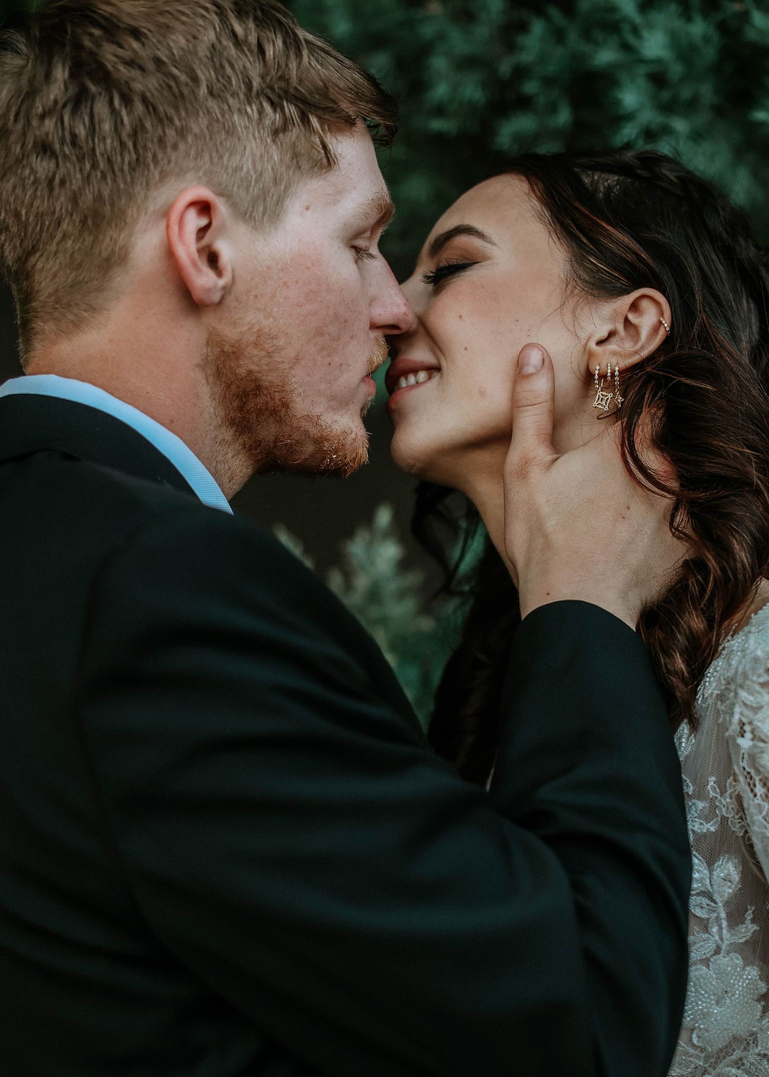 A bride and groom share a romantic almost-kiss moment, with the groom tenderly holding her face at their wedding.
